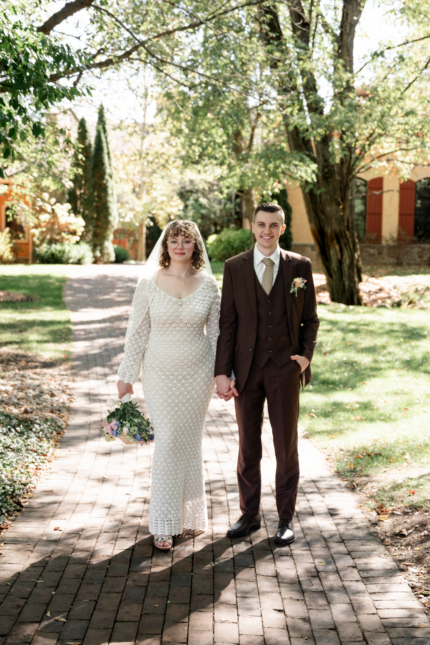 Wedding couple on brick path, bride in lace dress and groom in brown suit.