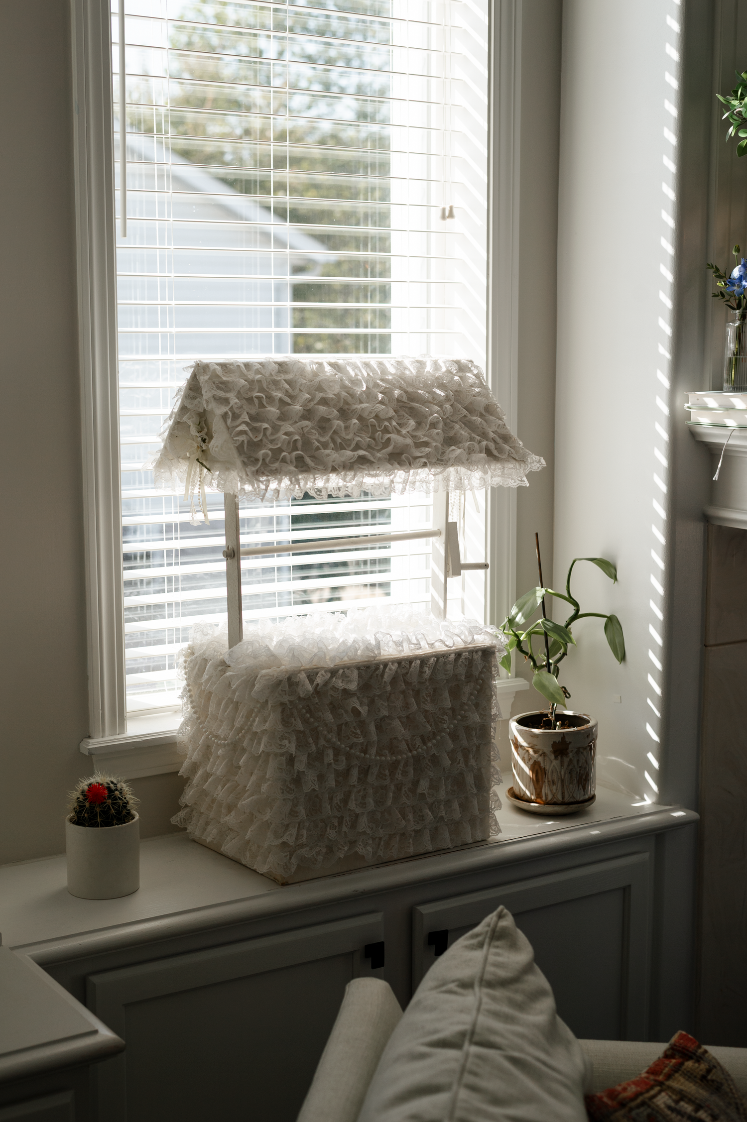 Sunlit windowsill with white blinds and small potted plants creating a cozy indoor garden atmosphere.