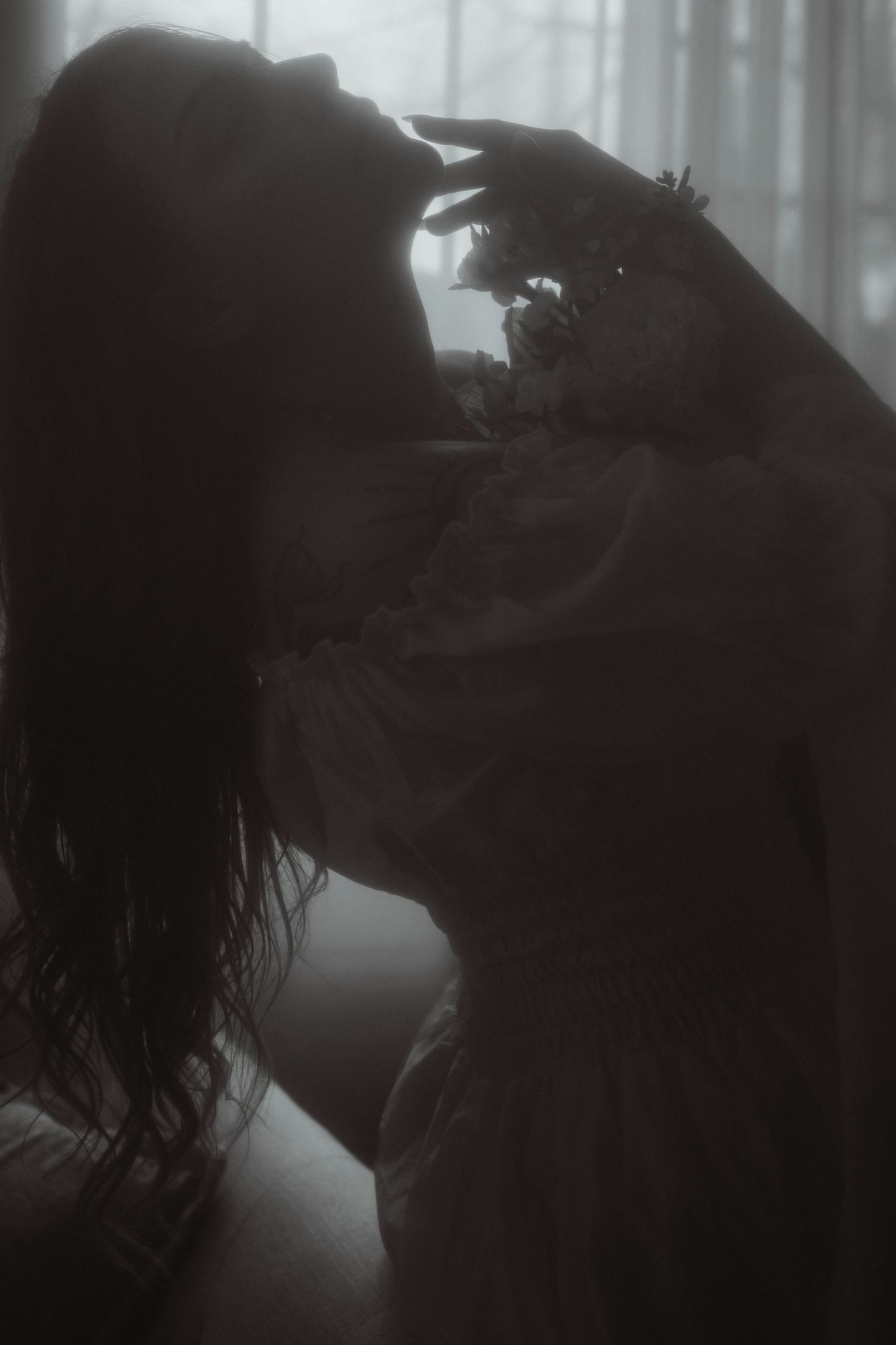 Dramatic dark silhouette of woman holding flowers, moody black and white fine art photography.