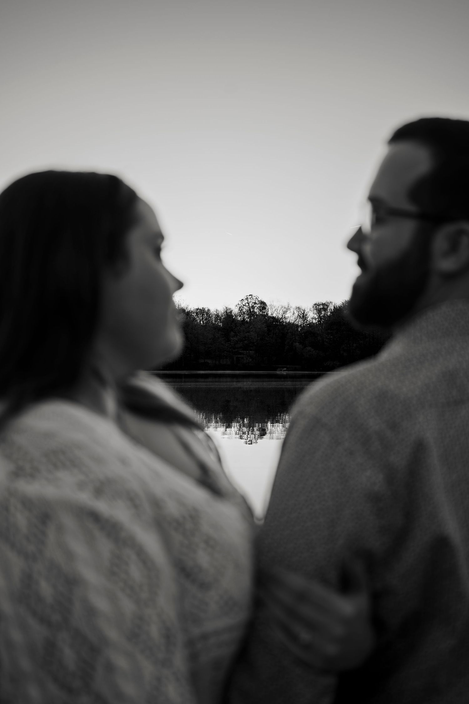 Black and white silhouette of a couple facing each other by a calm lake at dusk.