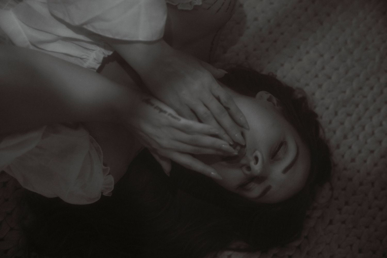 Black and white photo of a person lying down covering their face with their hand in a dramatic pose.