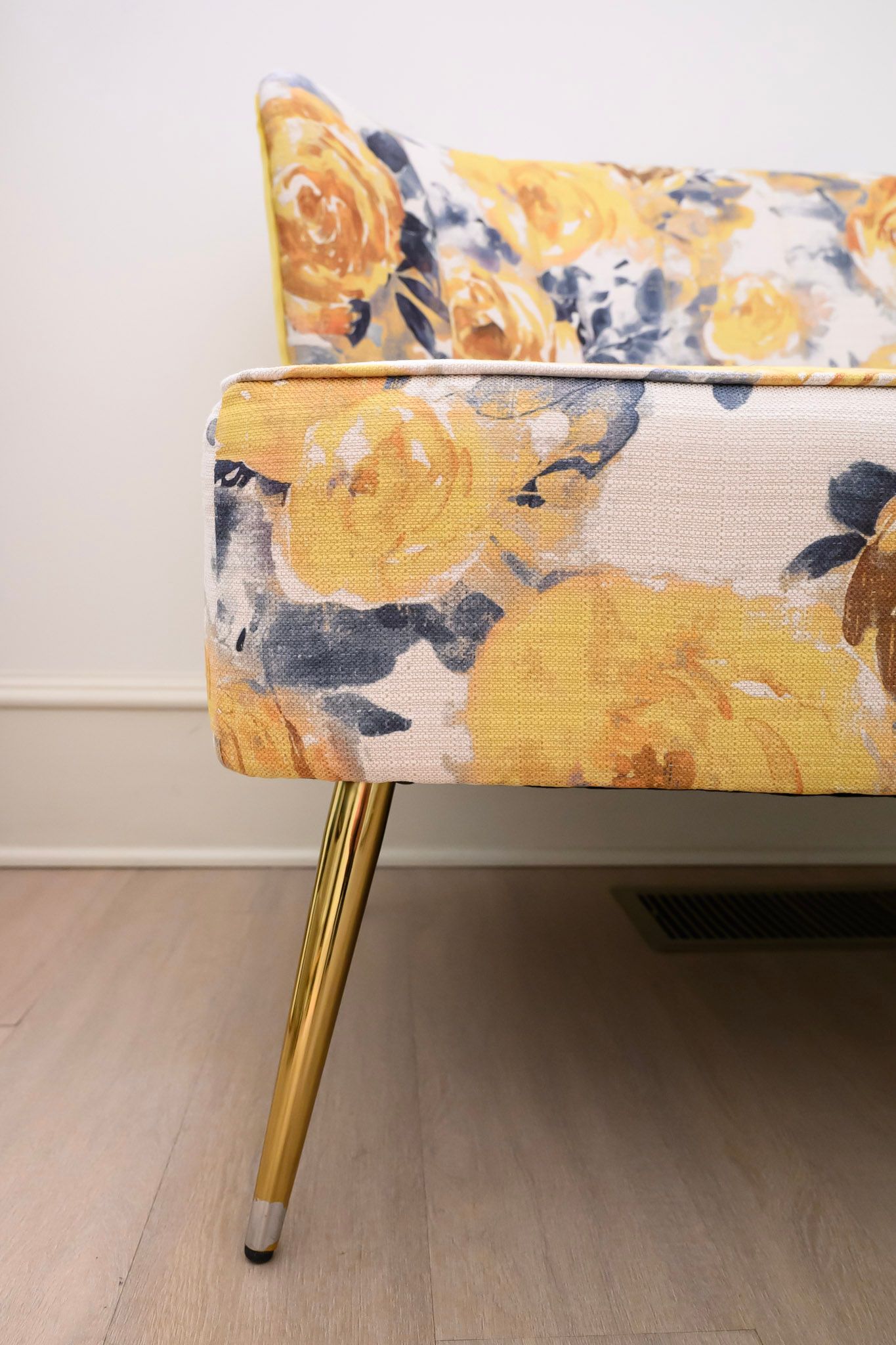 Close-up view of a floral upholstered sofa leg with gold metallic finish on hardwood flooring.