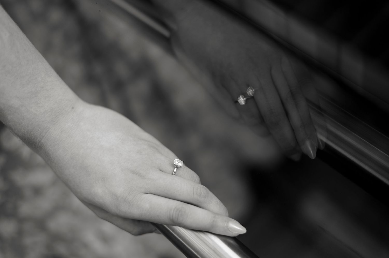 Black and white close-up photograph of a hand wearing an engagement ring resting on a surface.