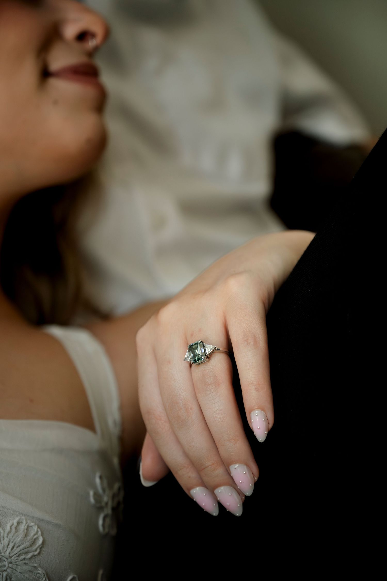 Close-up of a bride's hand displaying an elegant emerald-cut engagement ring with side stones on her ring finger.