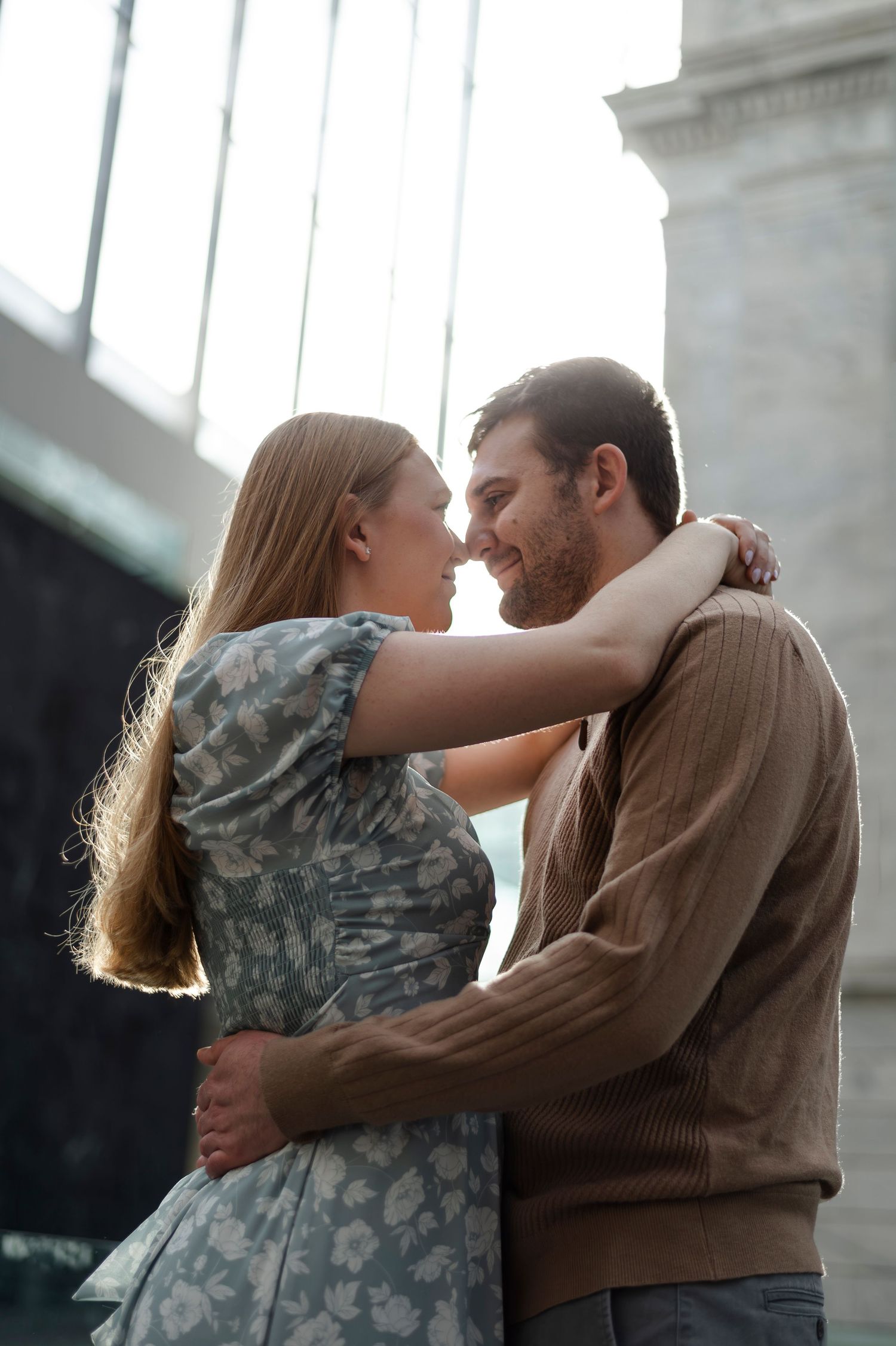 A smiling couple embraces and gazes at each other lovingly, woman in floral dress with arms around mans neck.