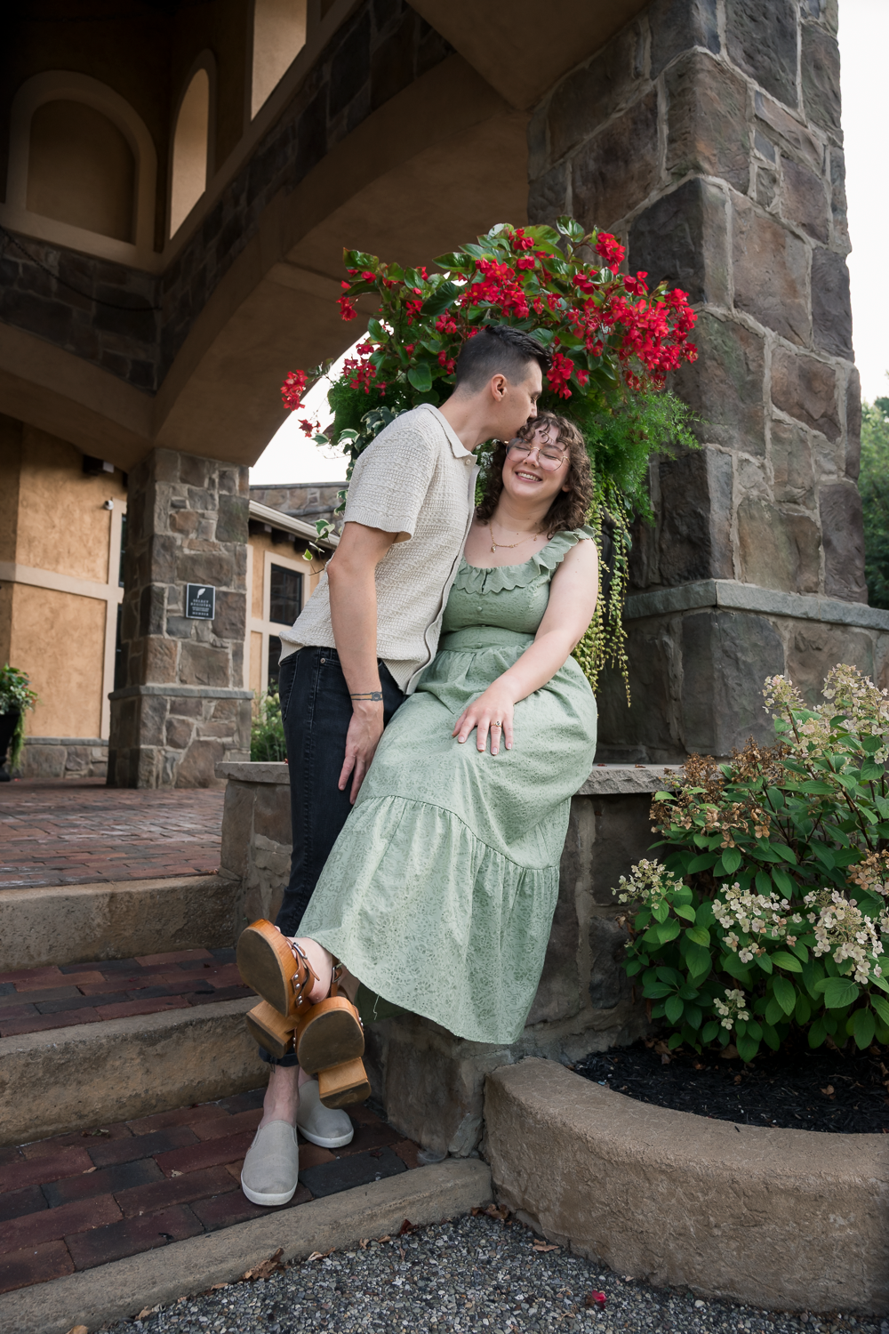 Couple sharing a tender moment on stone steps surrounded by red flowers and lush greenery.