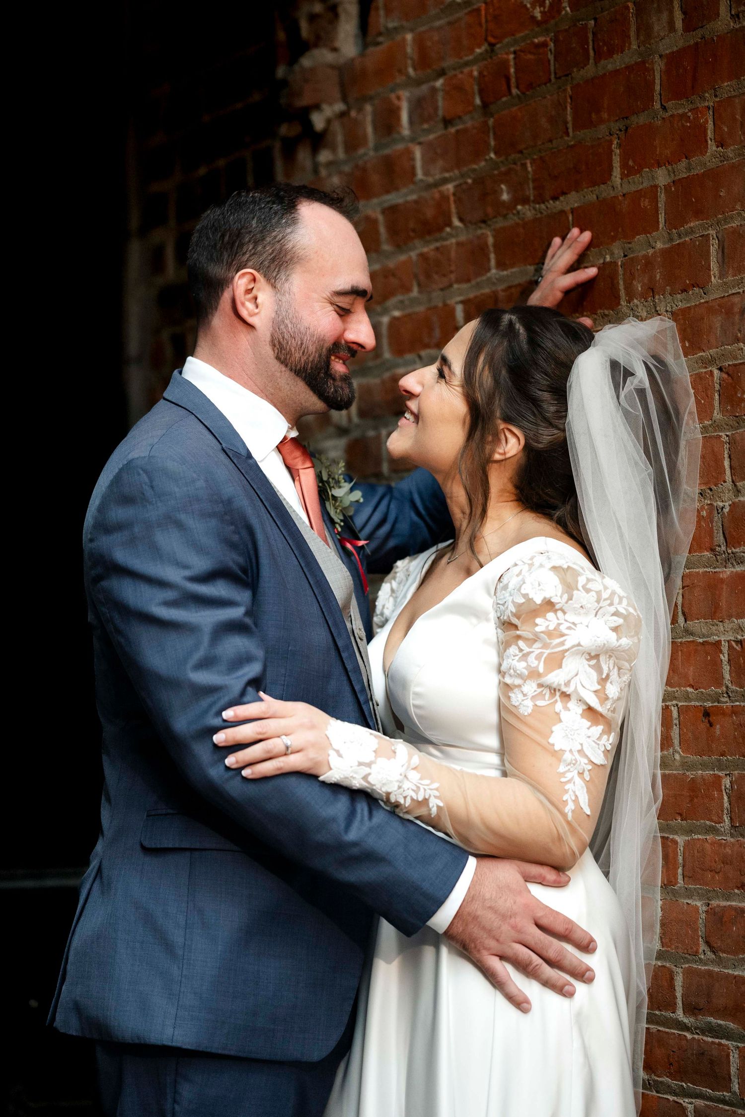 A romantic wedding moment captured against a rustic brick wall as a couple shares an intimate embrace.