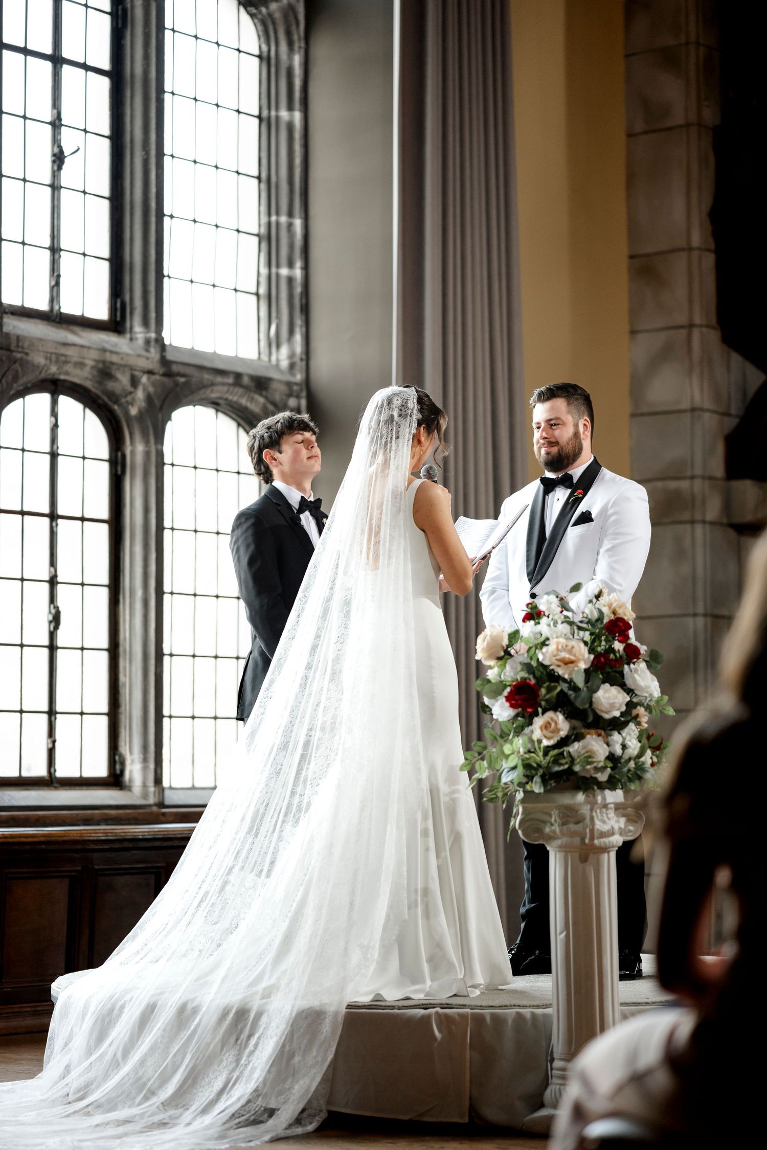 A bride and groom stand at the altar in a grand church, with the bride wearing a long white veil and the groom in a tuxedo.