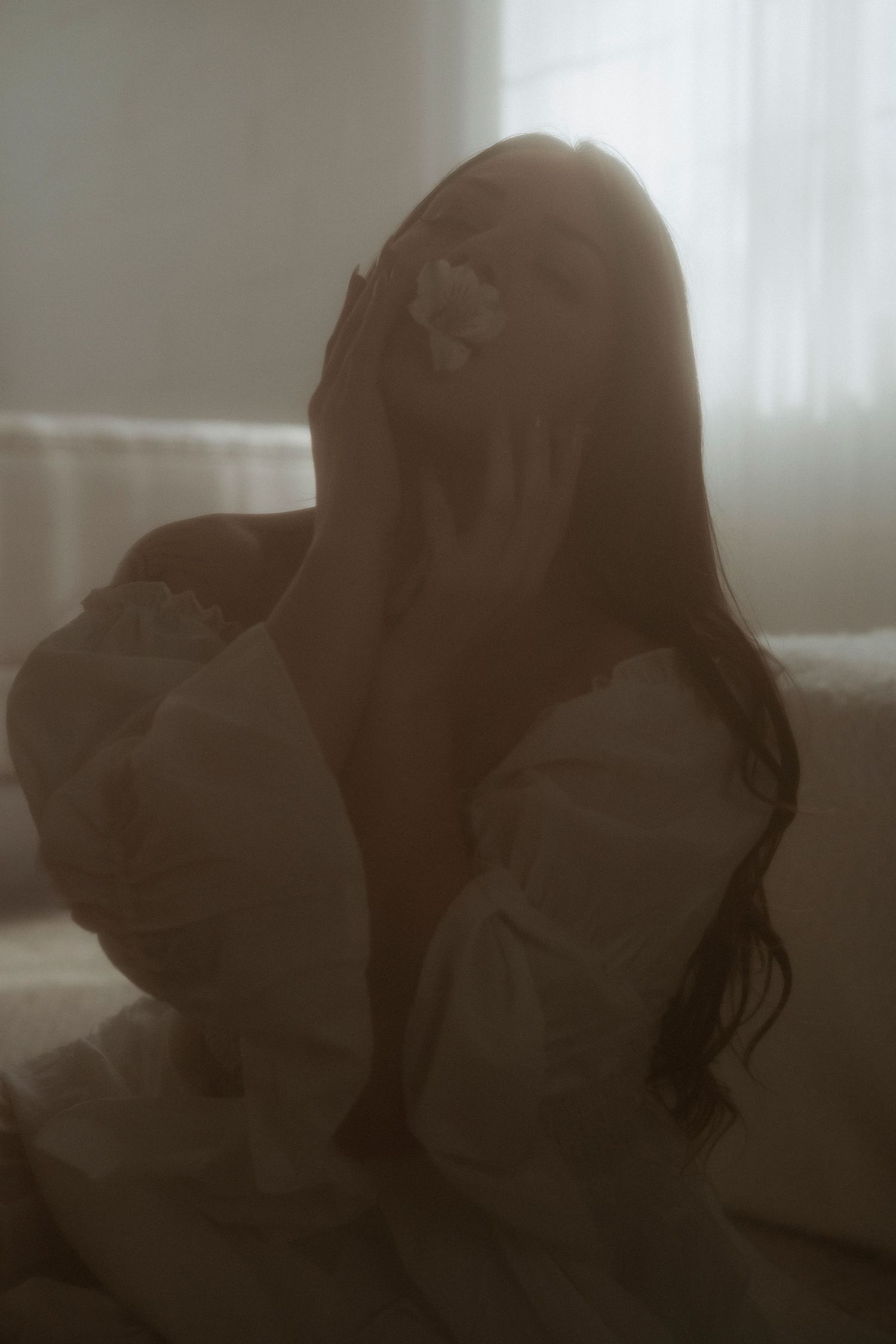 Ethereal silhouette of woman with long hair and flower accessory on white bed.