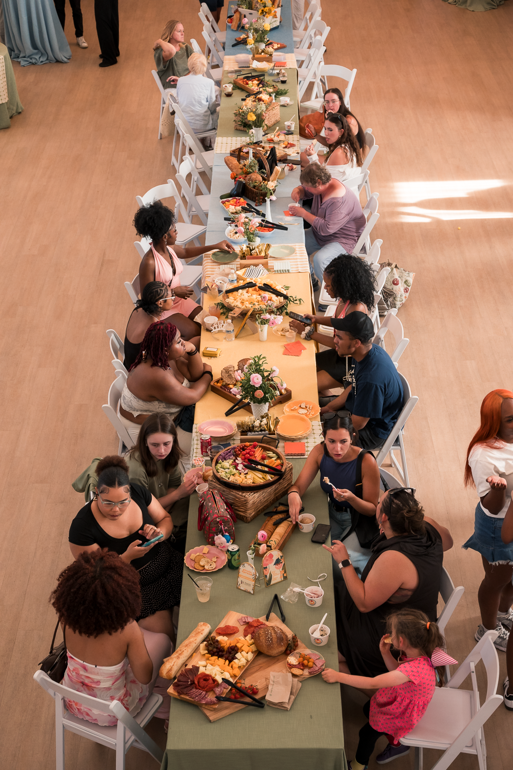Aerial view of diverse women gathered around a long banquet table filled with food and floral arrangements at an event.
