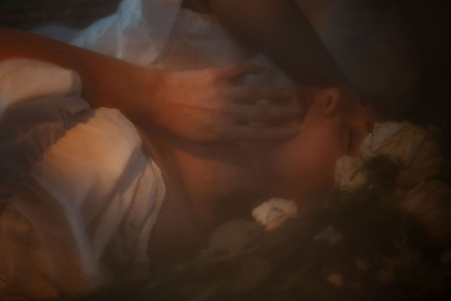 Soft moody portrait of a person lying among white flowers in dim, atmospheric lighting.
