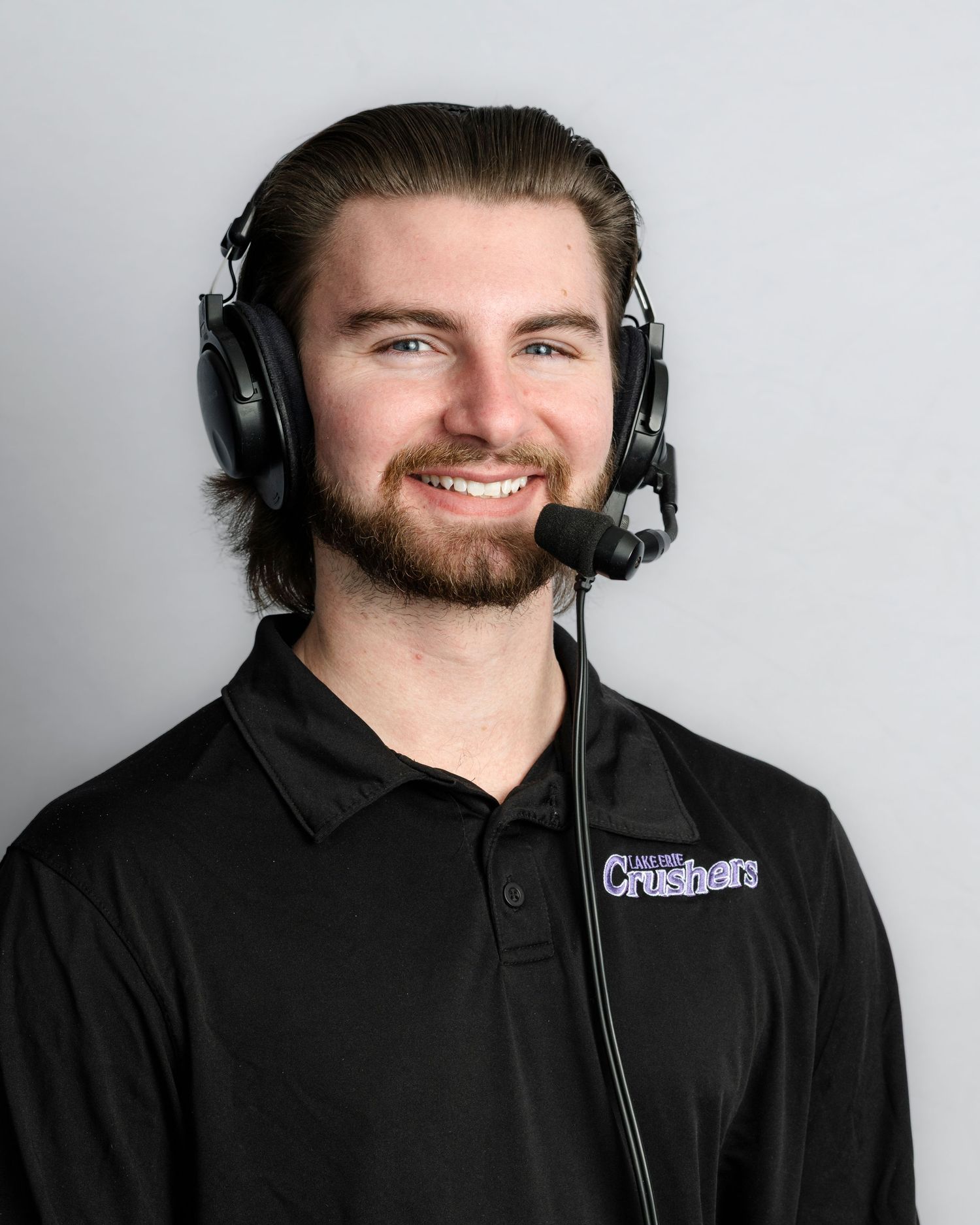 Person wearing black hoodie and headphones smiles against white background in professional headshot series.