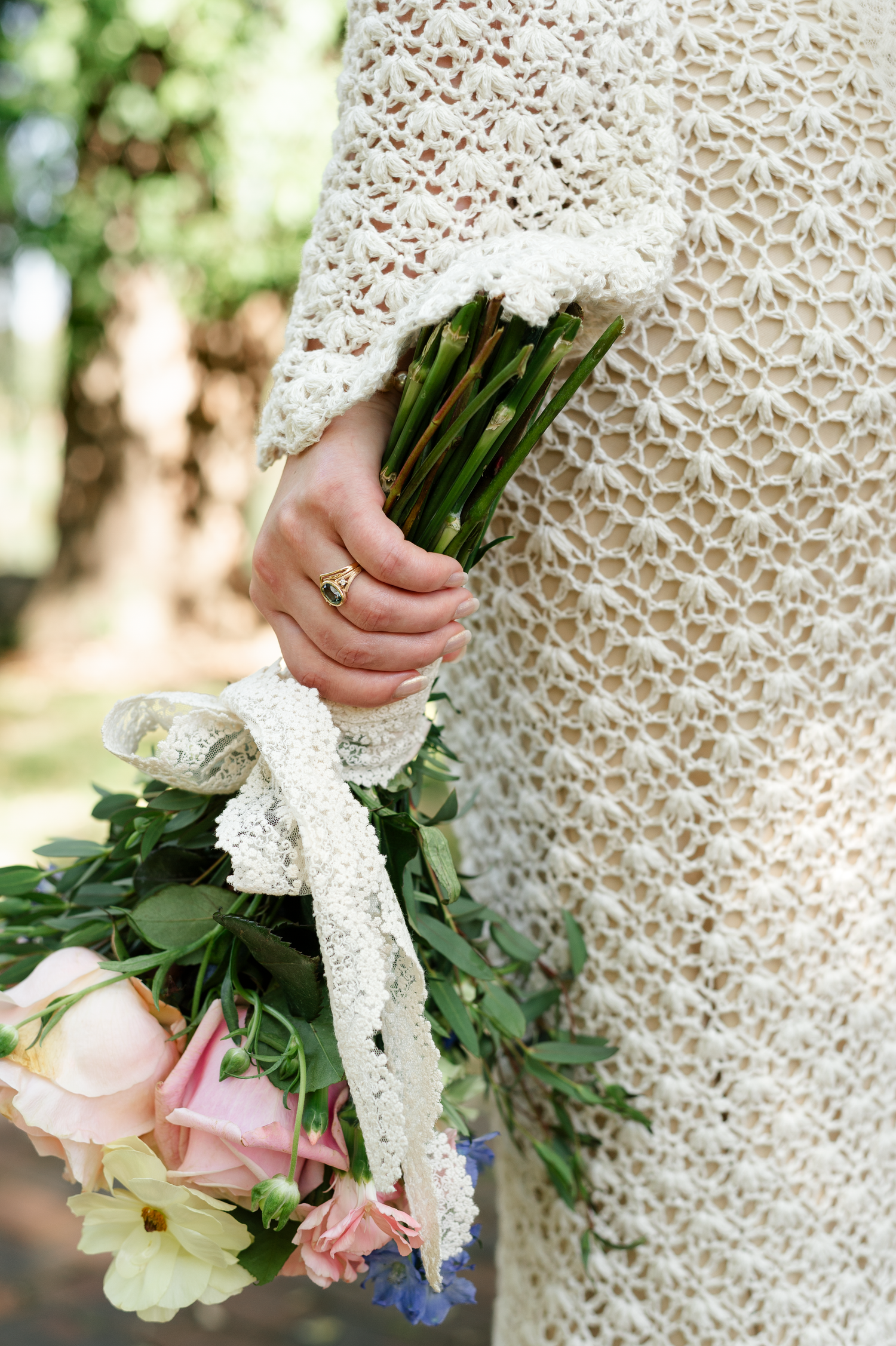Detail shot of lace wedding dress and pink rose bouquet with trailing ribbons.