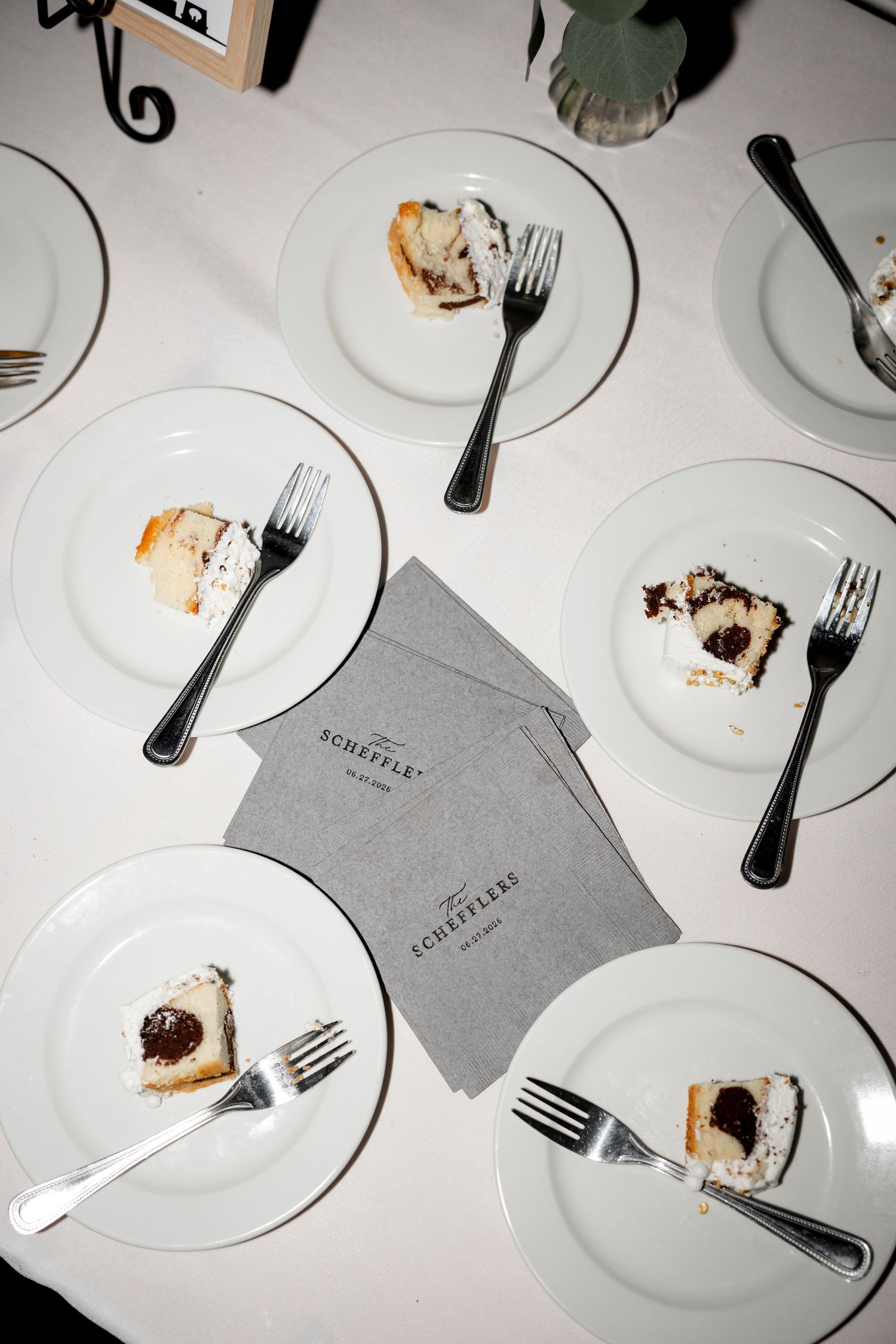 Overhead view of white dessert plates with cake slices and forks on a table with gray Scheffler napkins.