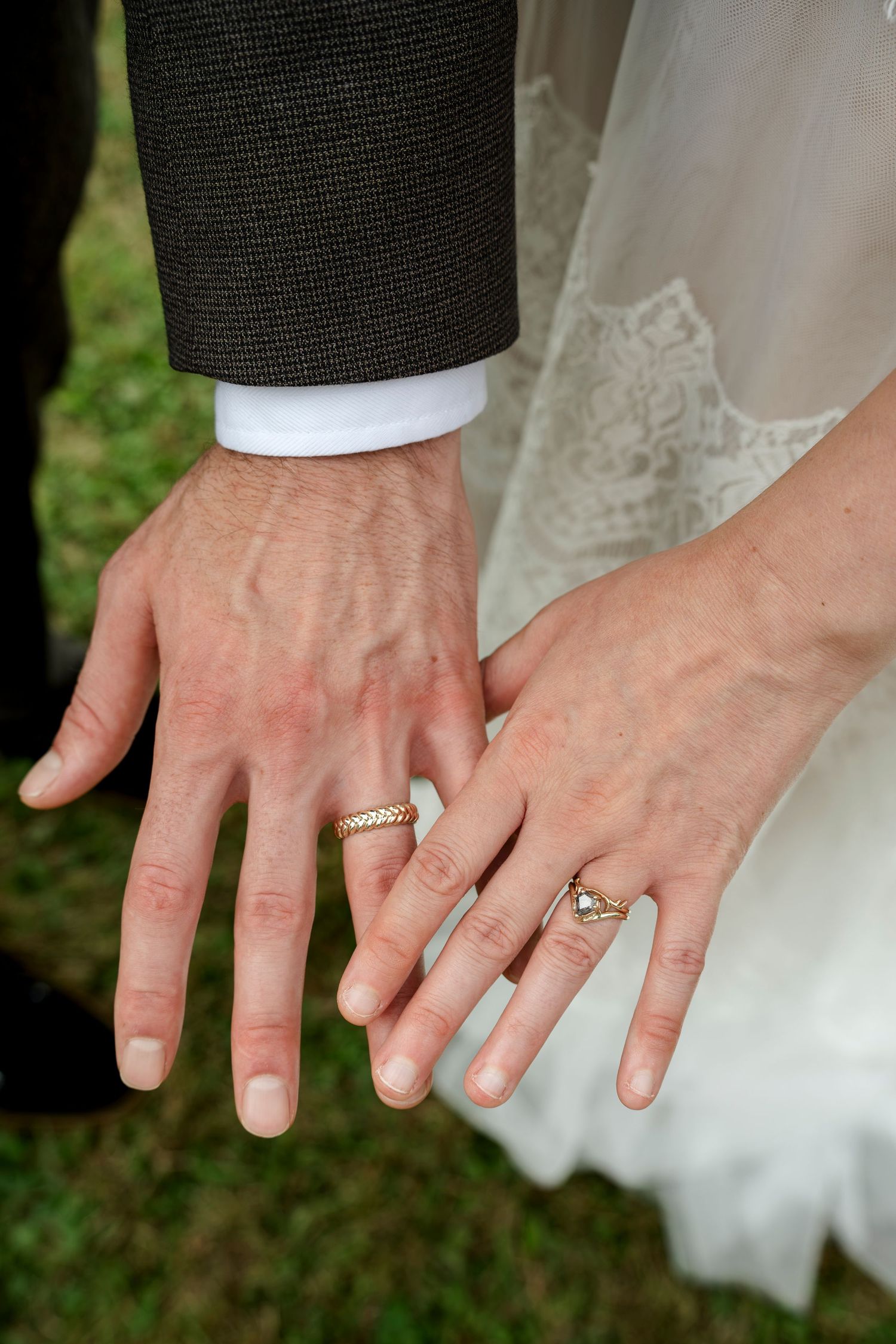 Newlywed couple displaying wedding rings on their hands, bride in lace dress and groom in gray suit.