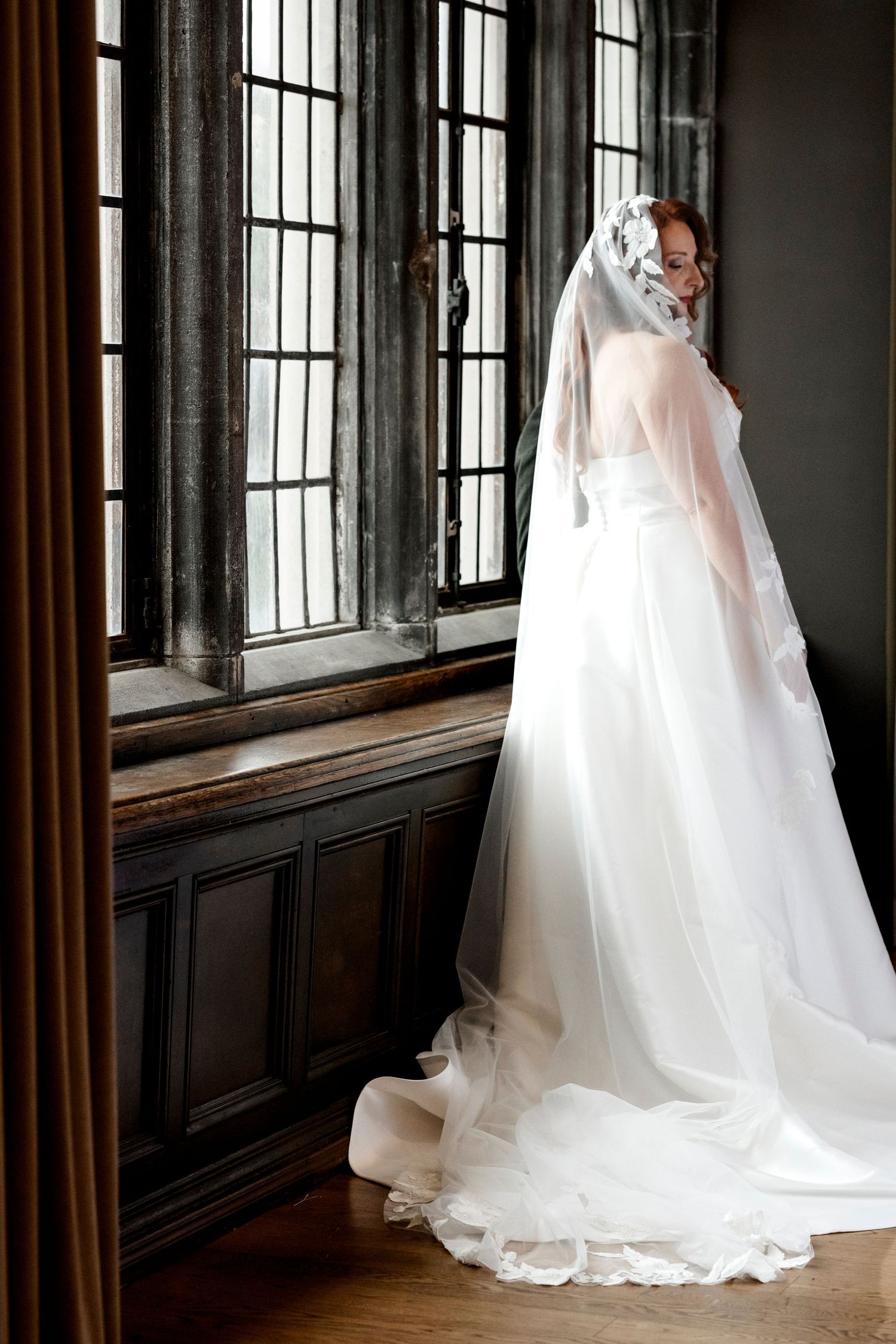 A flowing white wedding dress with a long train and veil photographed in sequence against dark wood paneled walls.