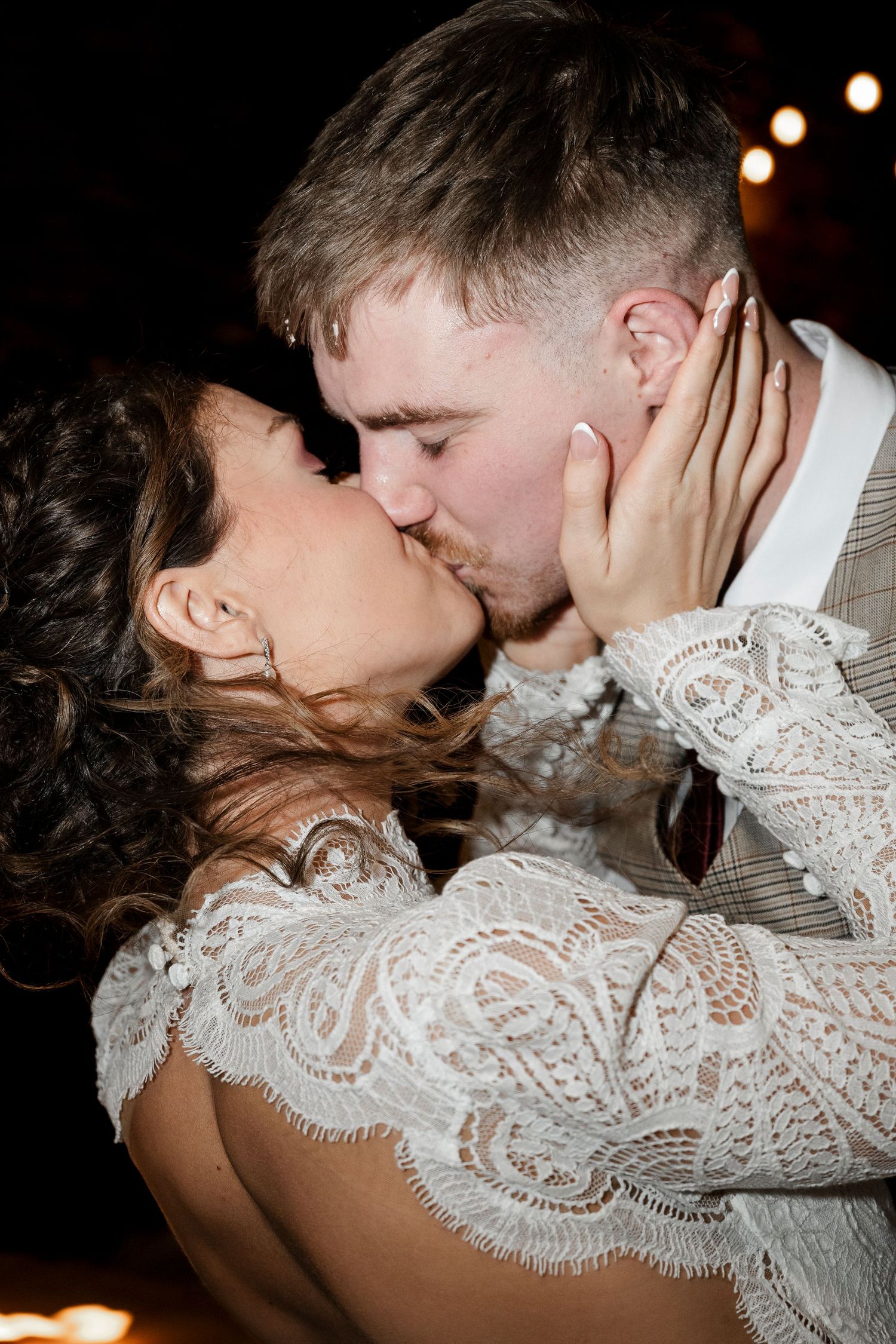 A romantic couple kissing passionately under the glow of fairy lights.