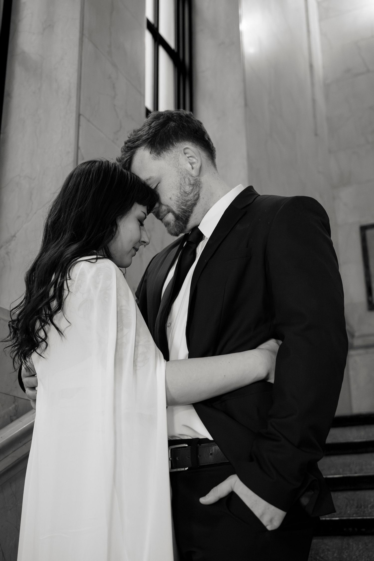 A series of four romantic black and white wedding photos showing a couple embracing and kissing on marble steps.