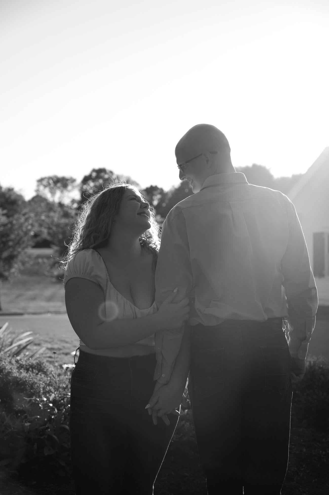 A silhouetted couple embraces in a romantic outdoor setting with sunlight creating a dreamy backlit effect.