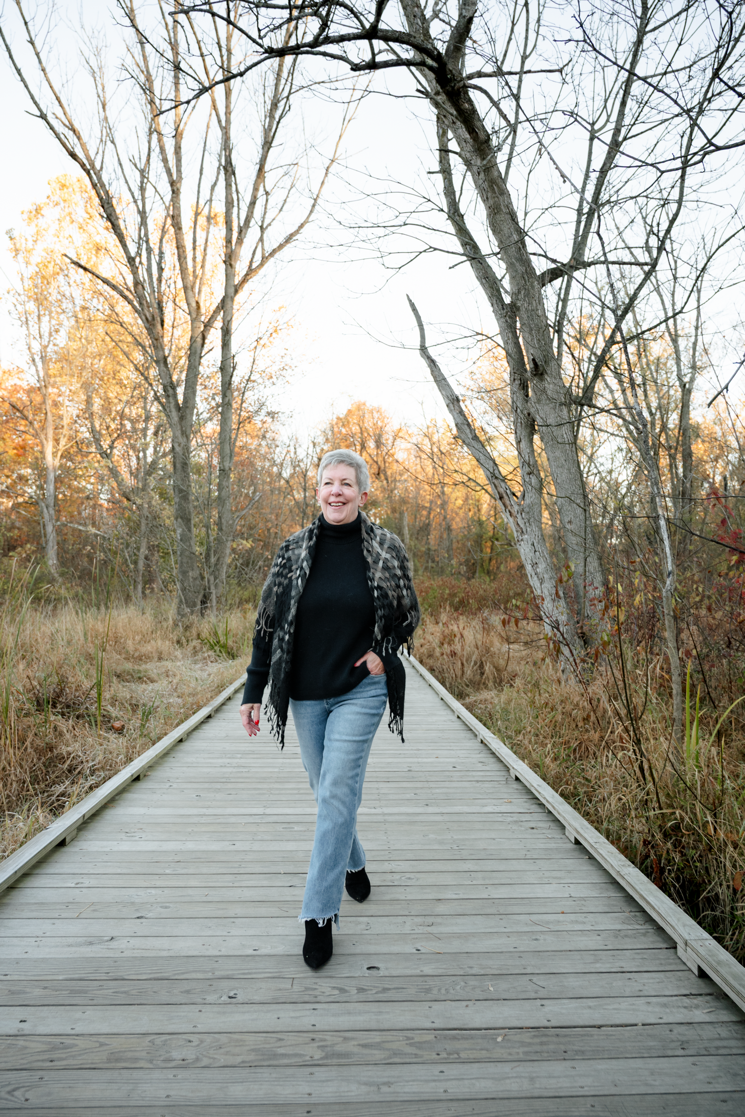 Person walking along a wooden boardwalk surrounded by autumn trees.