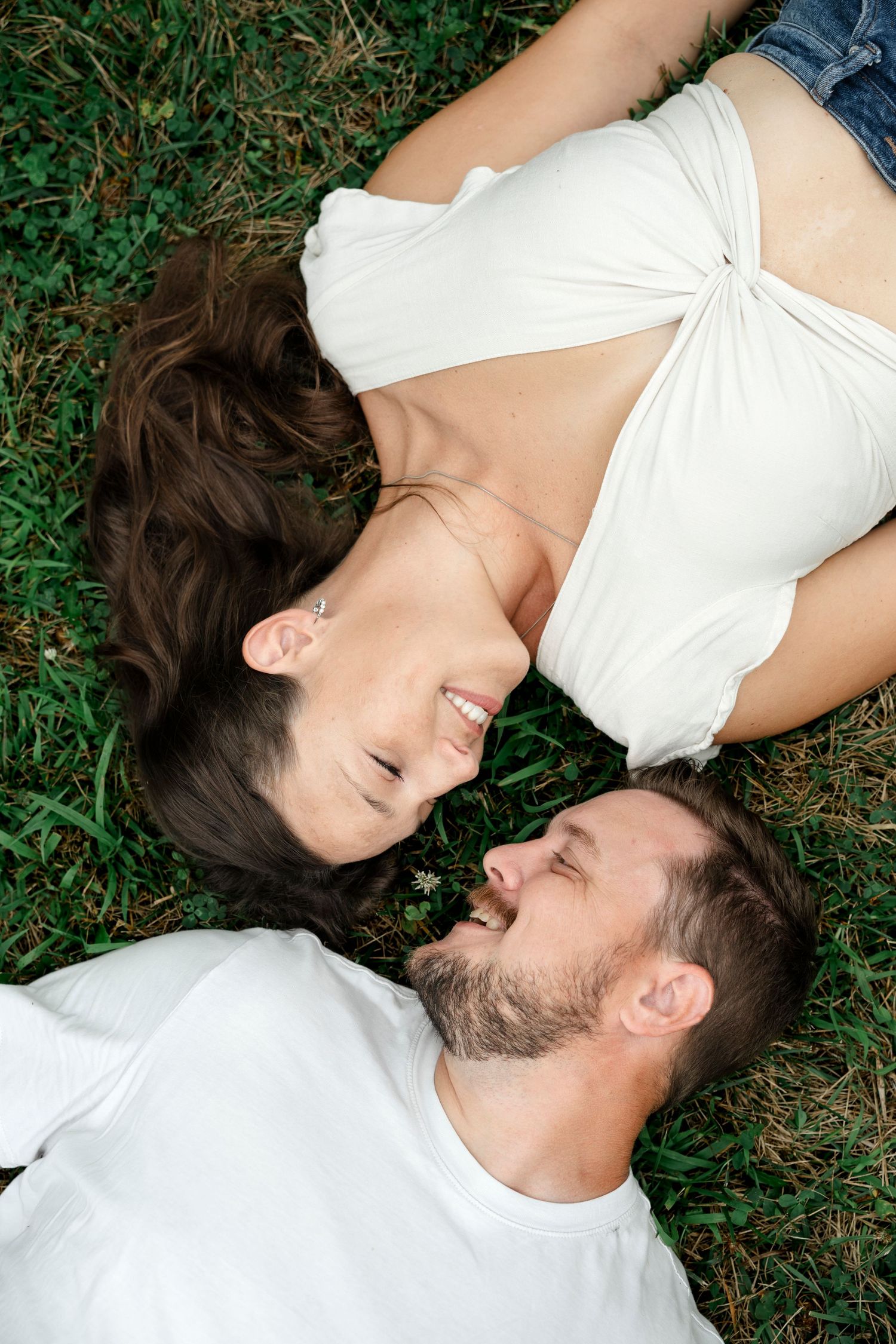 Happy couple lying on green grass, smiling and facing each other on a sunny day.