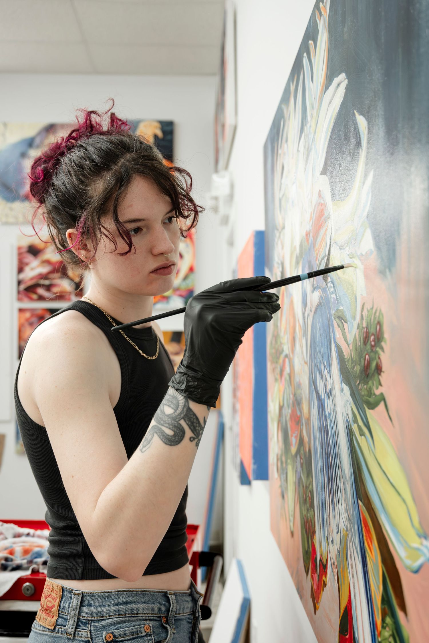 Artist works on large wall mural wearing black sleeveless top and denim in bright gallery space.