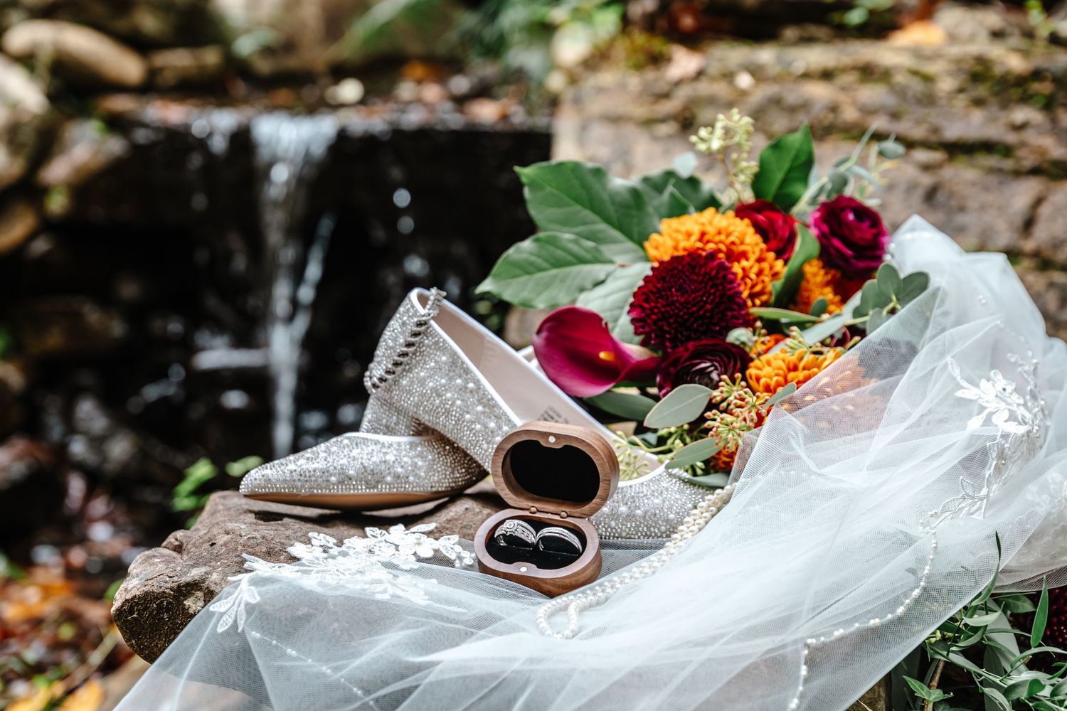 Close-up of wedding rings nestled among vibrant autumn flowers and white veil.