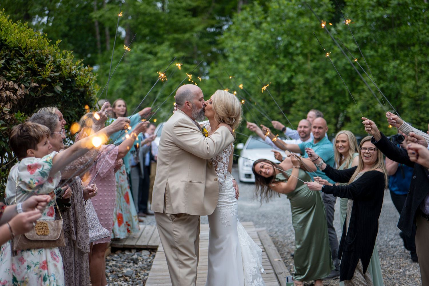 Wedding celebration with guests forming sparkler tunnel exit at twilight.