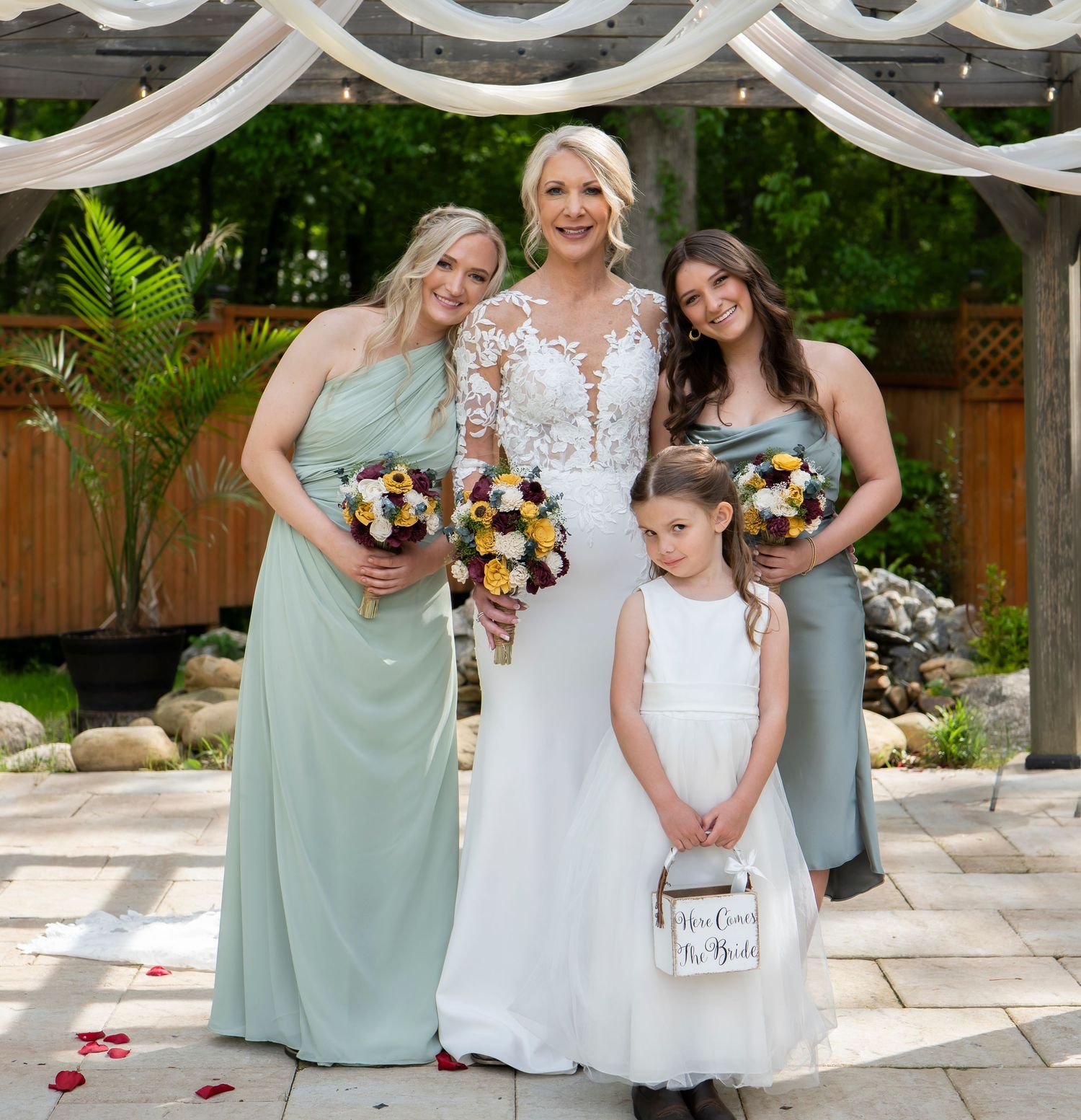 Wedding party in mint green dresses poses with couple under white draped arch.