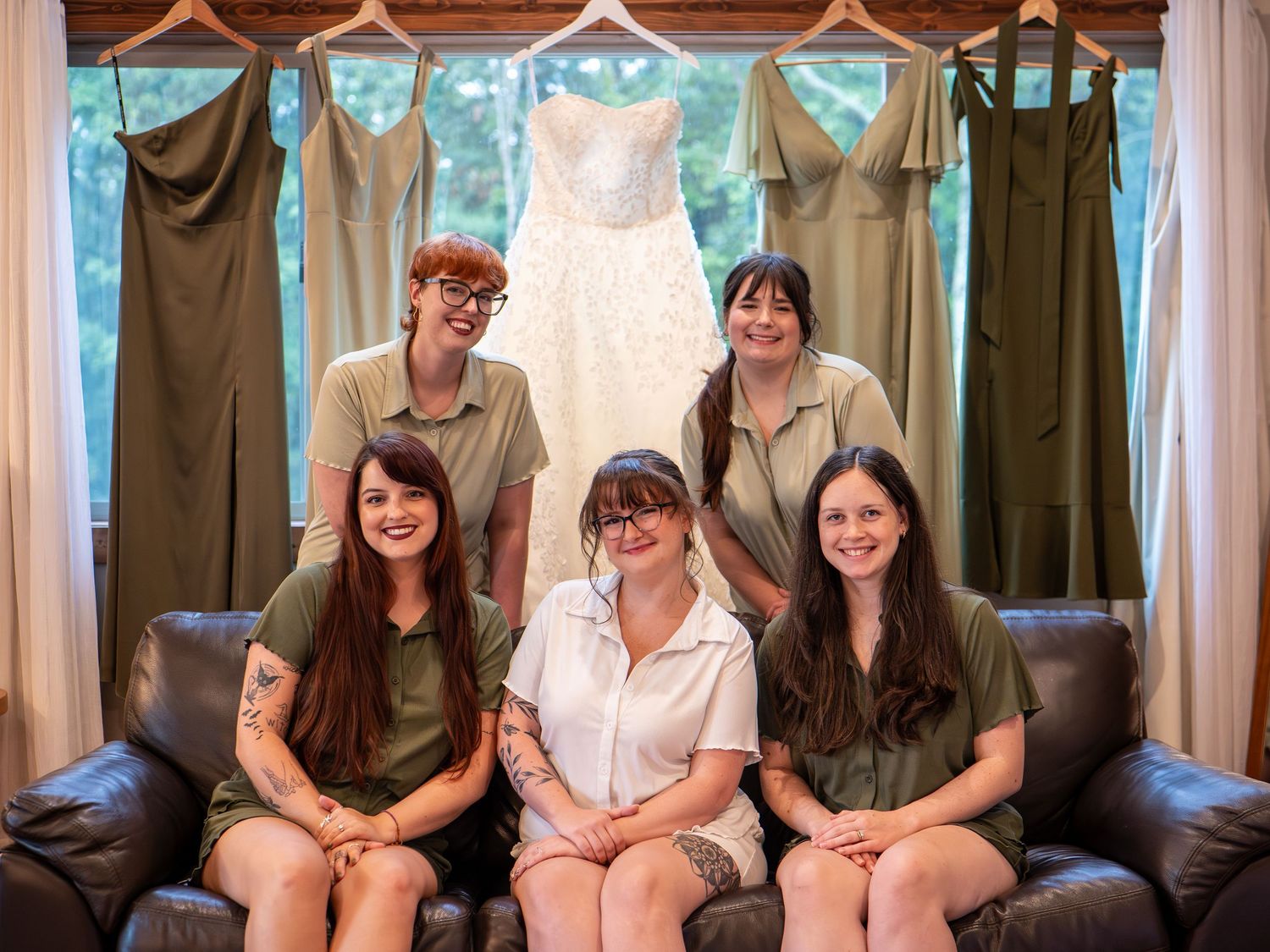 Wedding party gathered on couch with brown drapes and natural lighting.