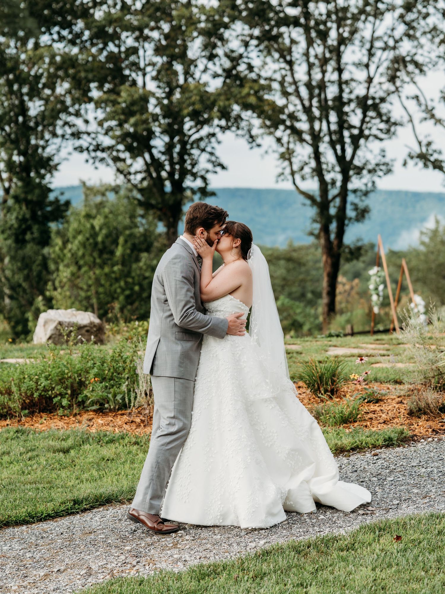 A romantic wedding photo series showing a couple embracing on a scenic hilltop path surrounded by greenery.