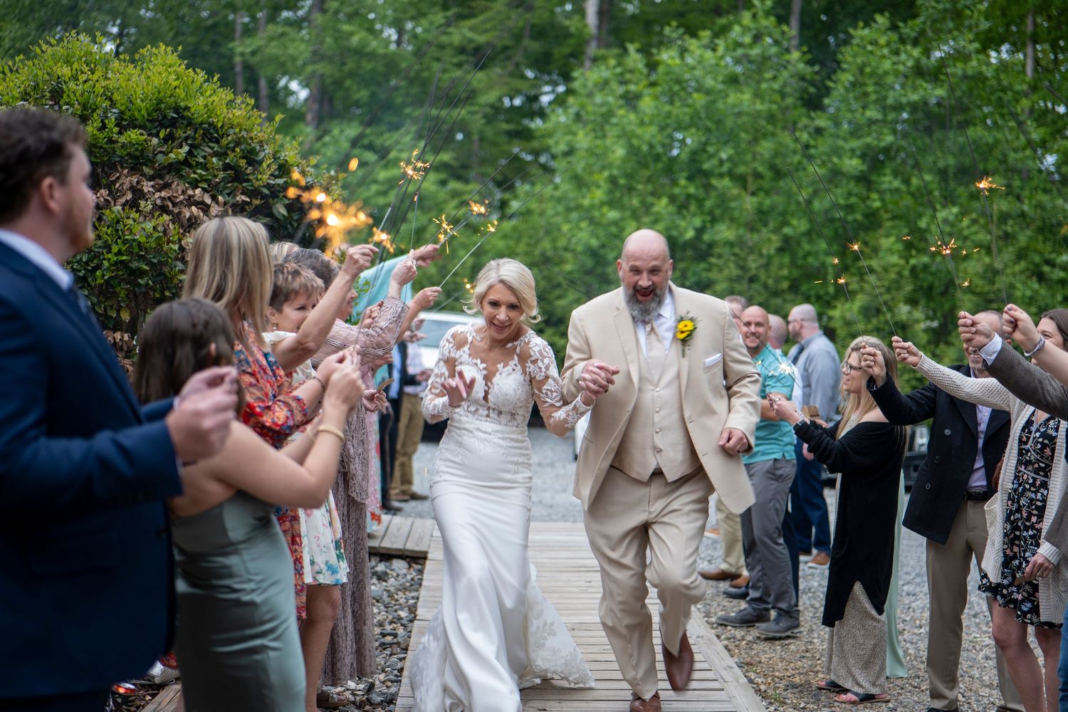 Joyful wedding exit with guests lining pathway holding sparklers at dusk.