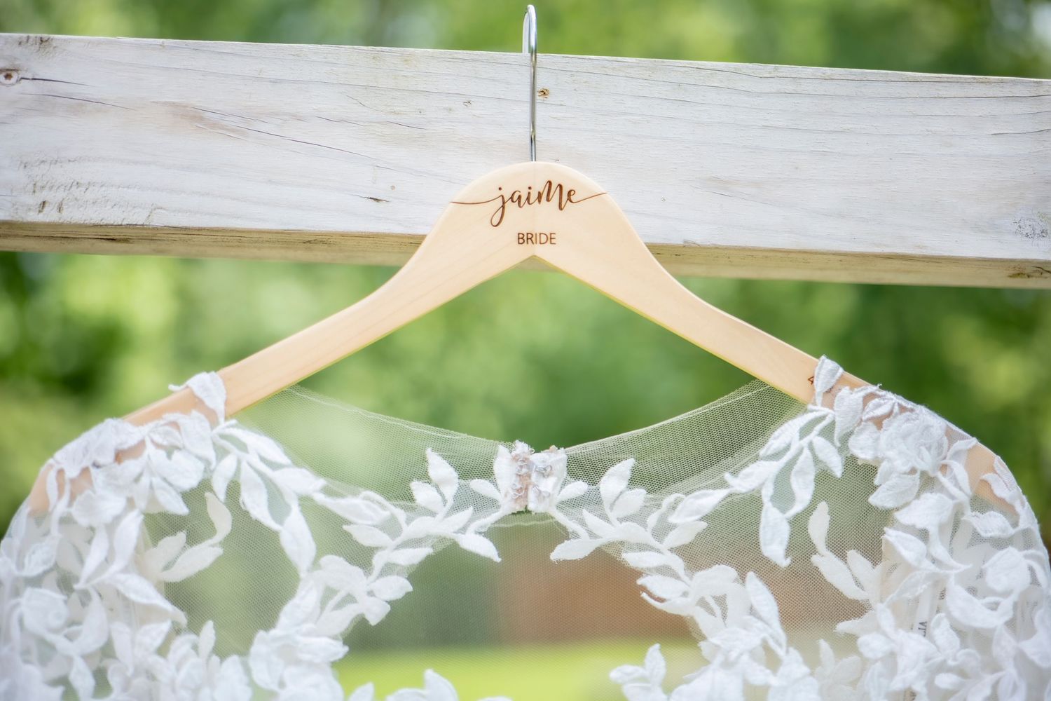 Elegant white lace wedding dress hanging on wooden hanger against natural background.