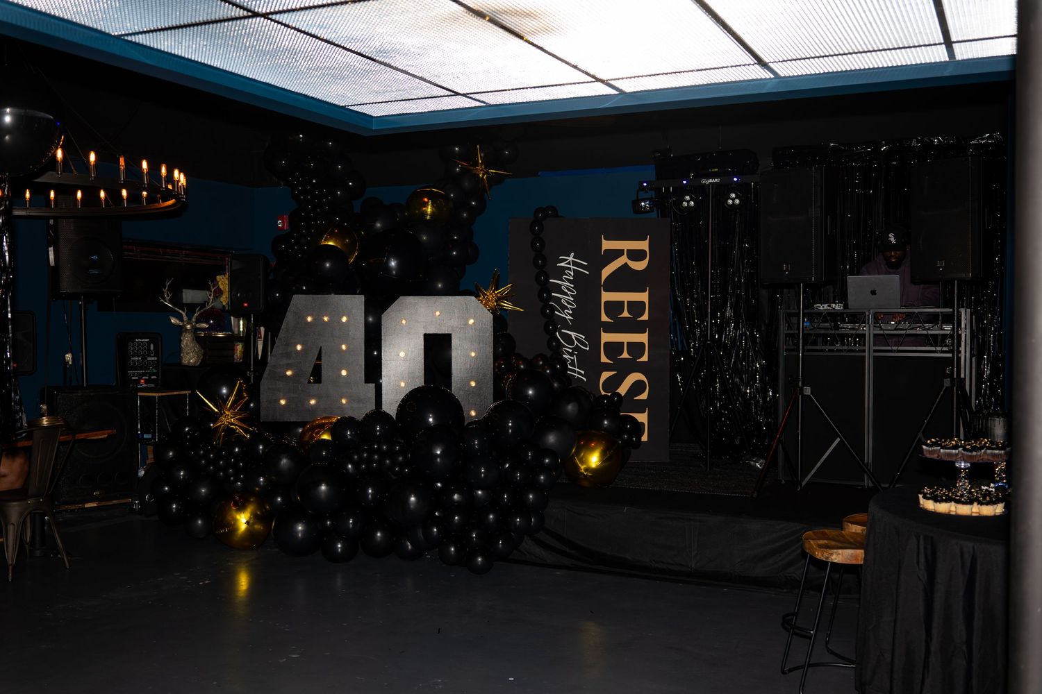 Elegant 40th birthday party setup with illuminated number balloons, black decor, and a personalized REESE banner.