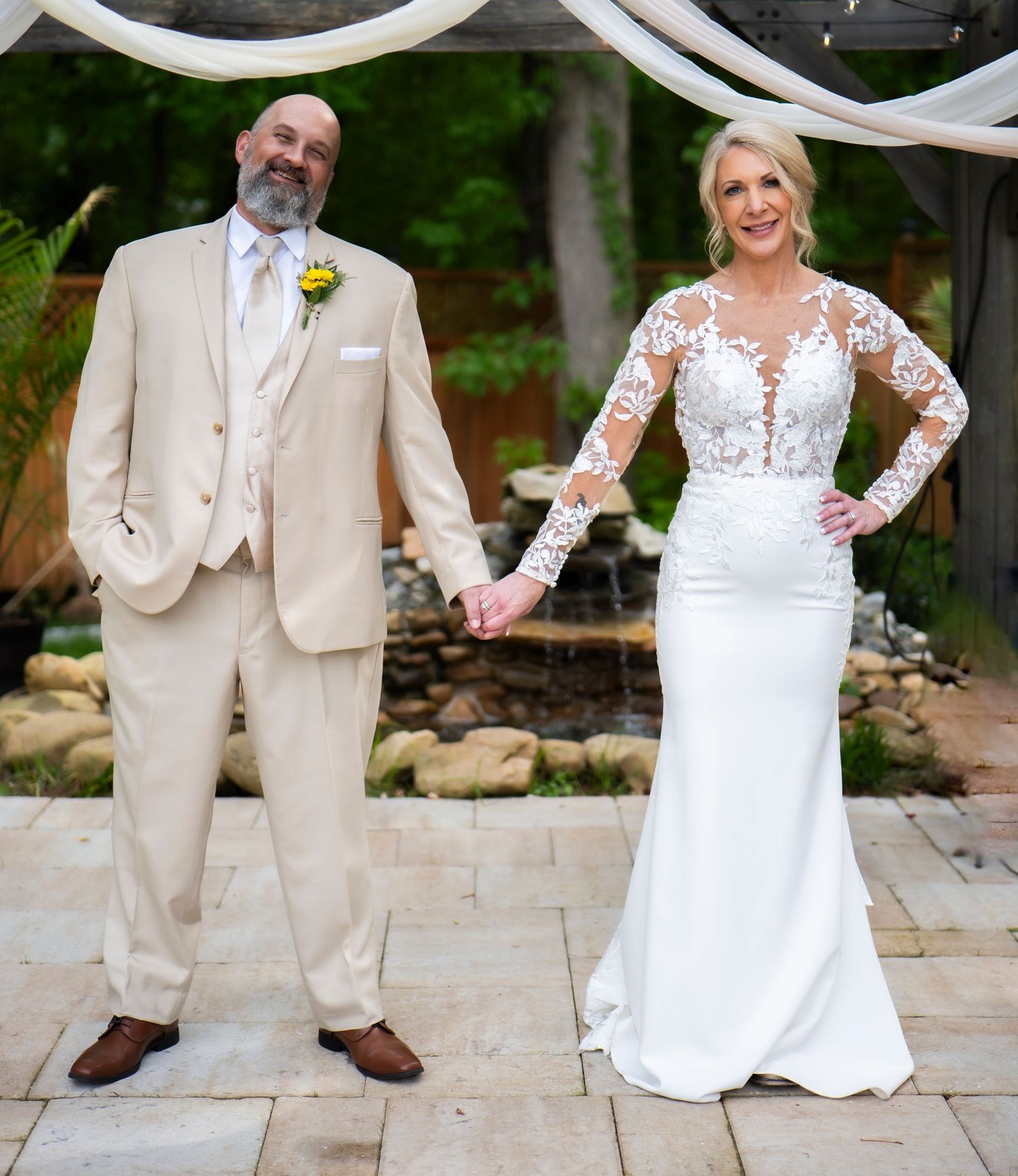 Newlyweds share intimate moments on stone patio with garden backdrop.