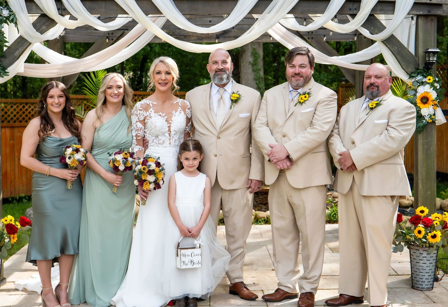Wedding party poses together in sage green and tan attire with sunflower accents.