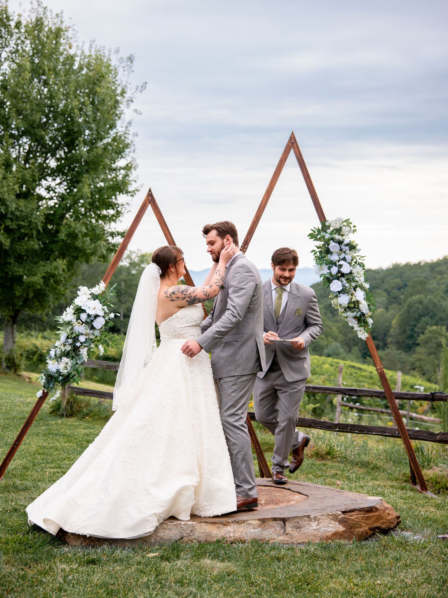 Wedding couple sharing intimate moments by a rustic wooden triangle arch in an outdoor setting.