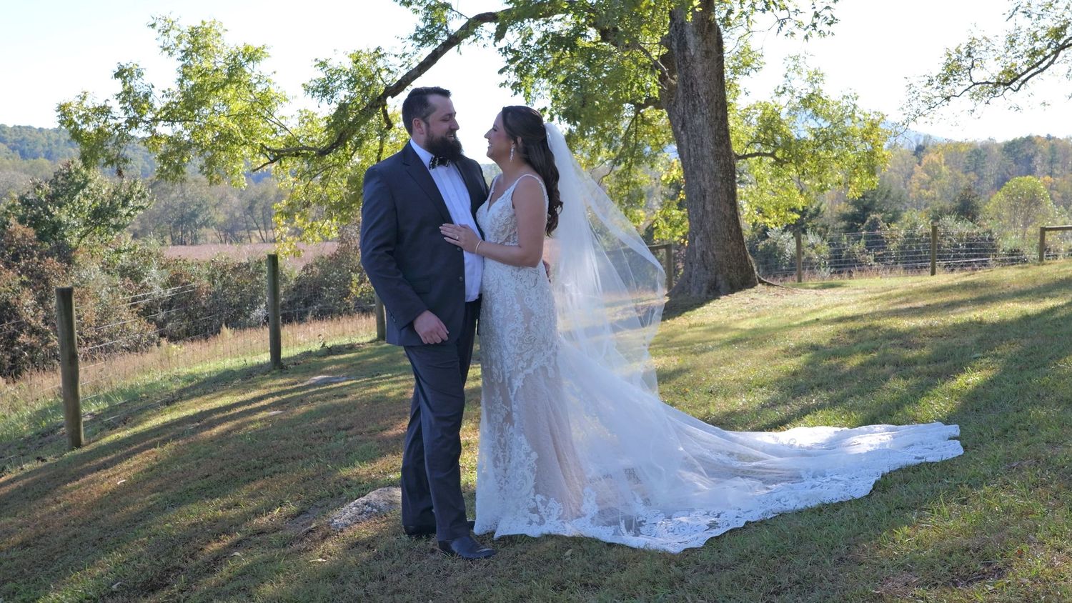 Wedding couple poses in front of a rustic white gazebo surrounded by lush green landscape.