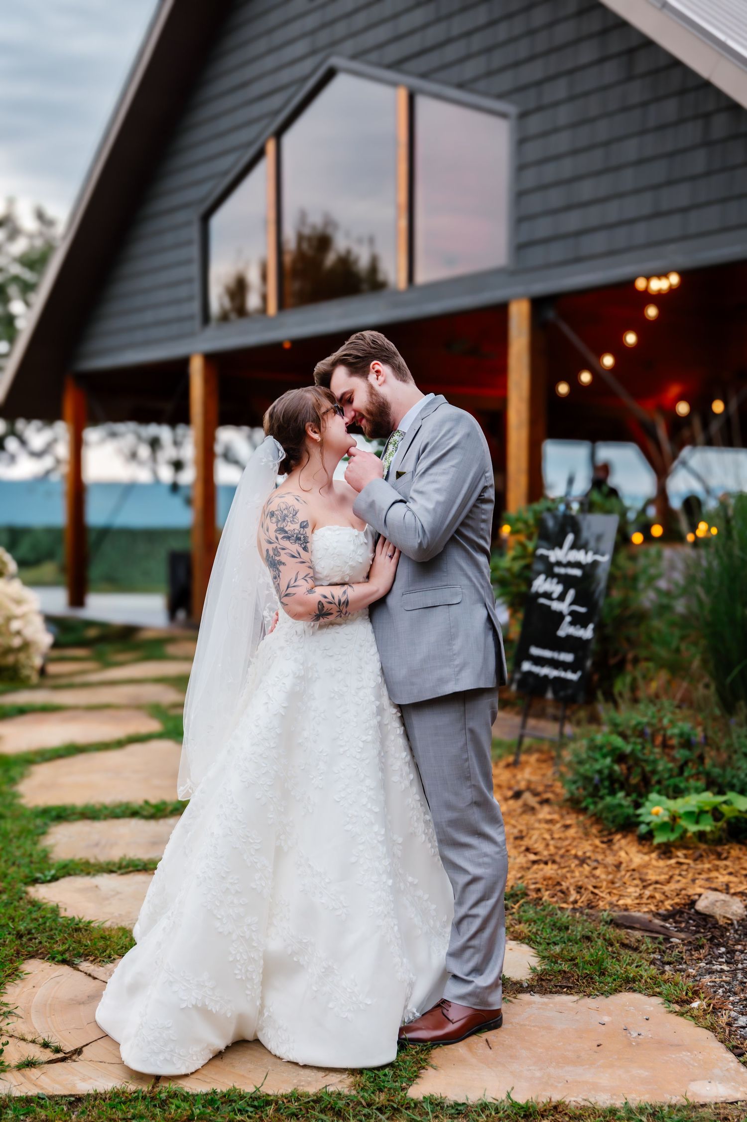 Evening wedding photos in front of a gray house with stone pathways and string lights.