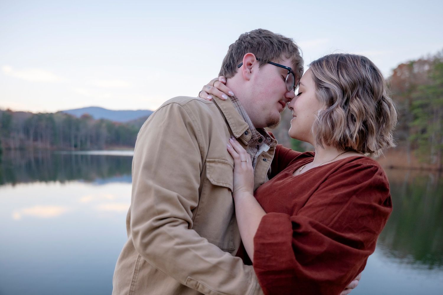 A tender moment captured against a scenic lake backdrop with fall foliage.