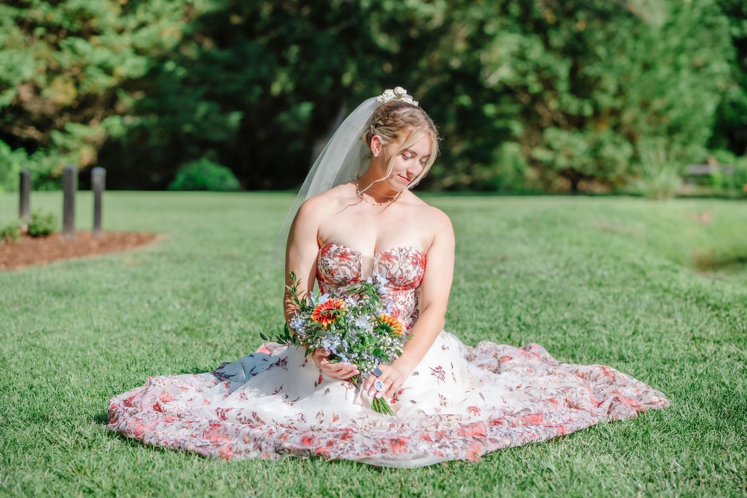 Bride in floral wedding dress poses gracefully on manicured lawn.