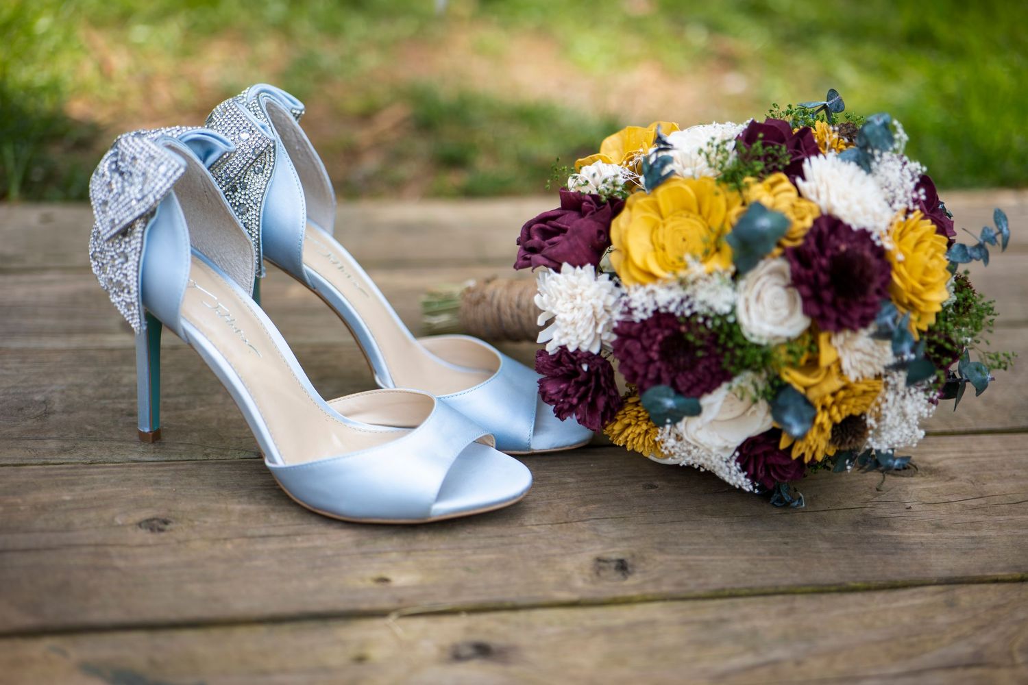 Light blue wedding heels next to a colorful bouquet with yellow and purple flowers on wooden surface.