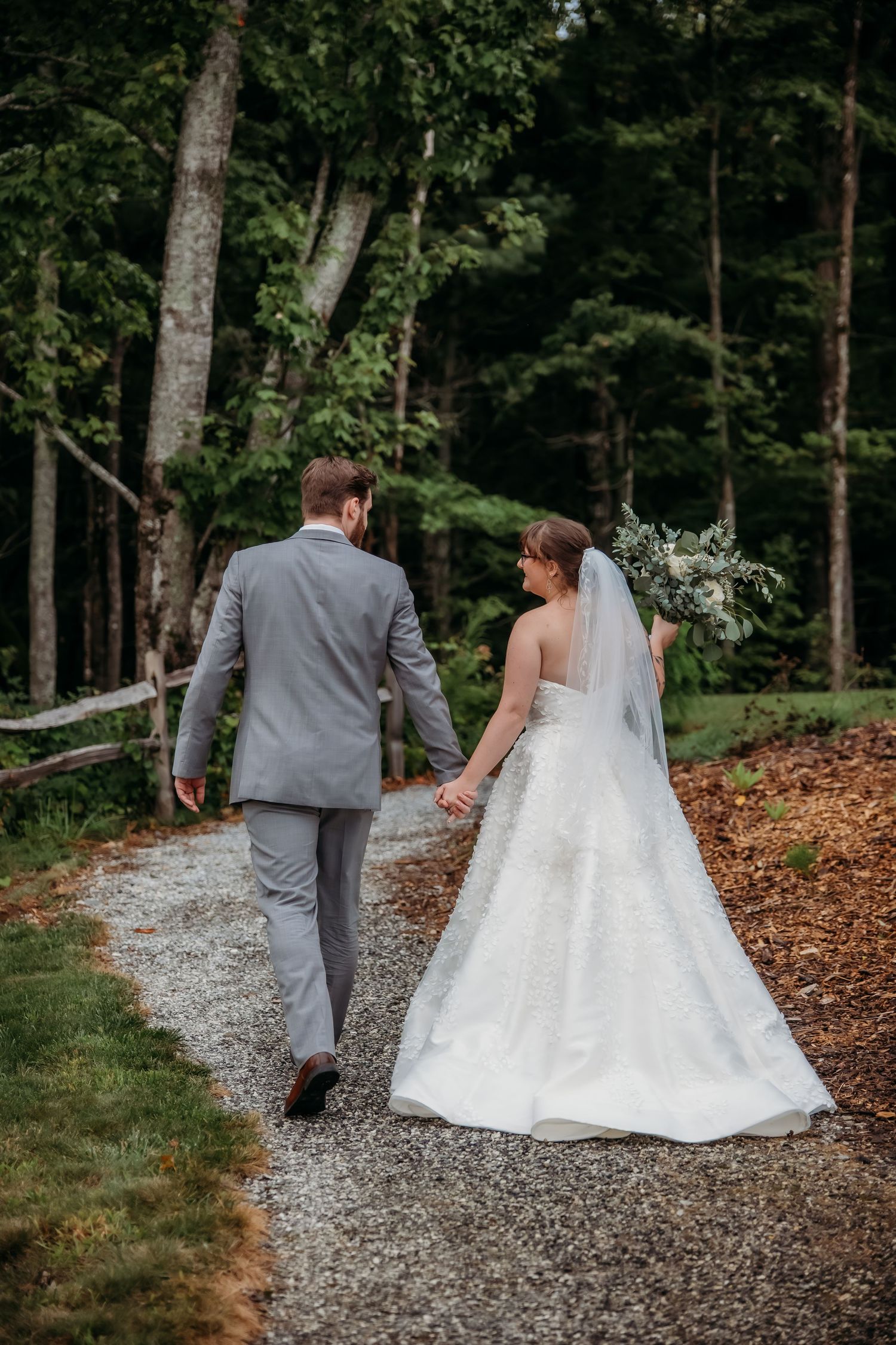 Couple walking together down a gravel path through a wooded area after their wedding ceremony.