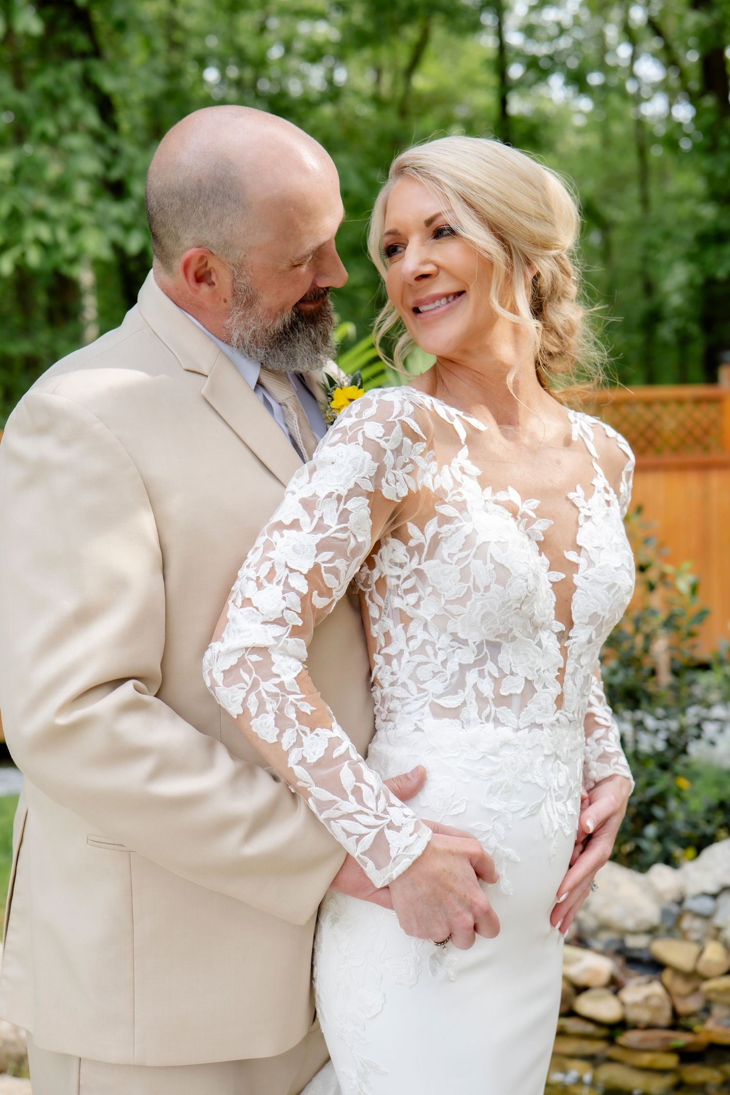 Romantic outdoor wedding portraits with lace dress and tan suit in garden setting.