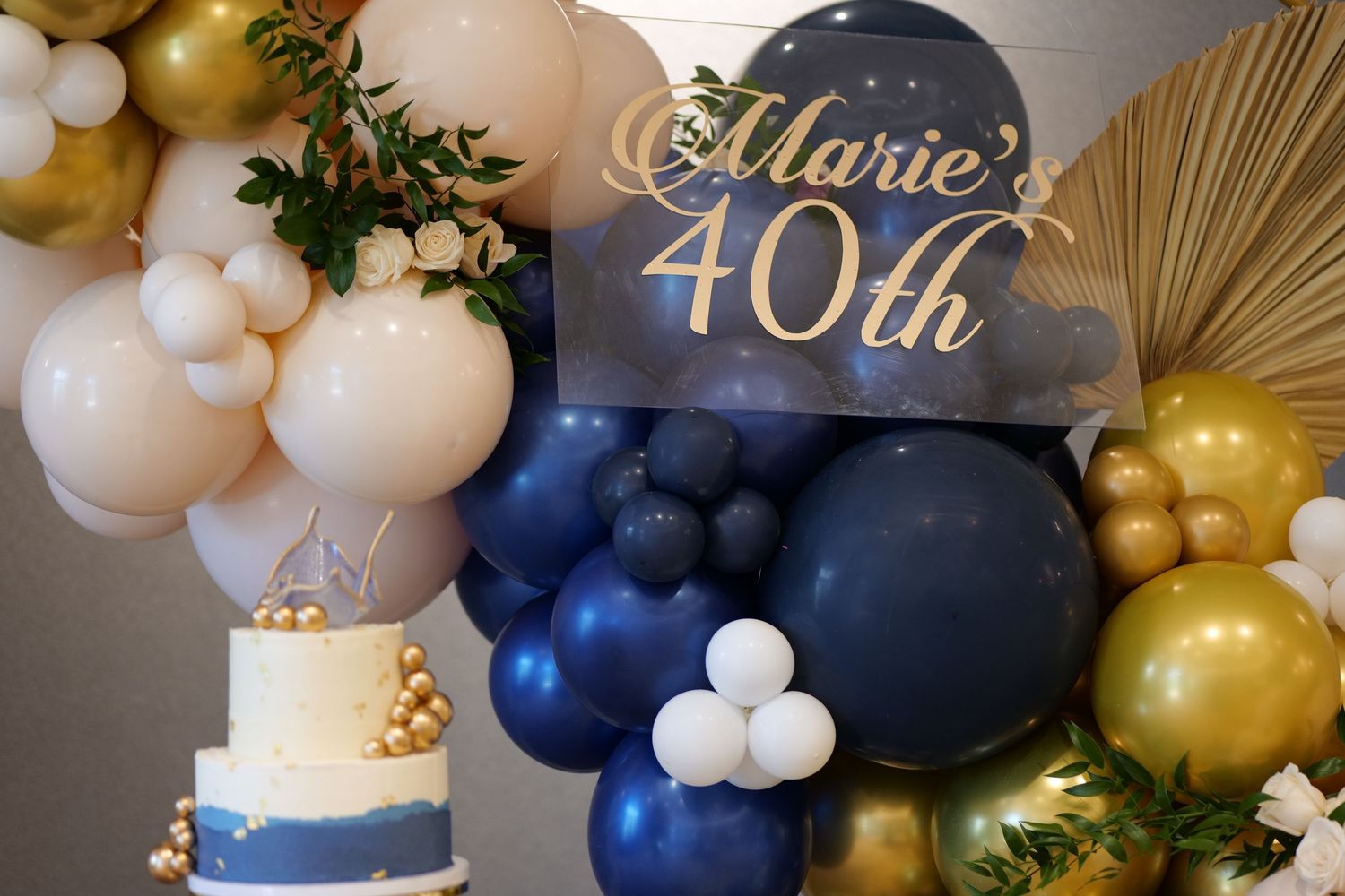 Marie's 40th birthday party decor with navy, gold, and cream balloon garland, a two-tier cake, and elegant signage.