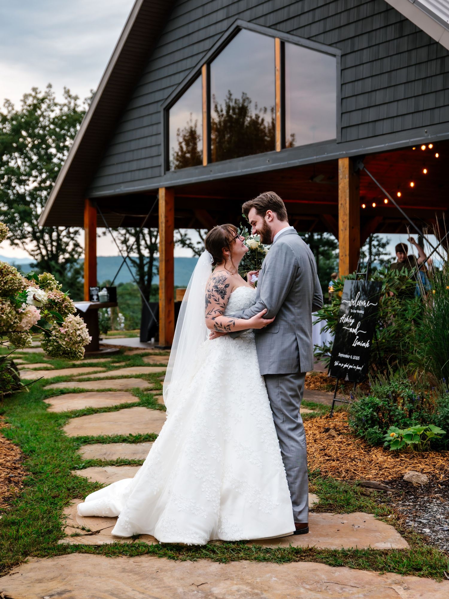 Romantic outdoor wedding ceremony at a rustic cabin venue with stone pathway and string lights.