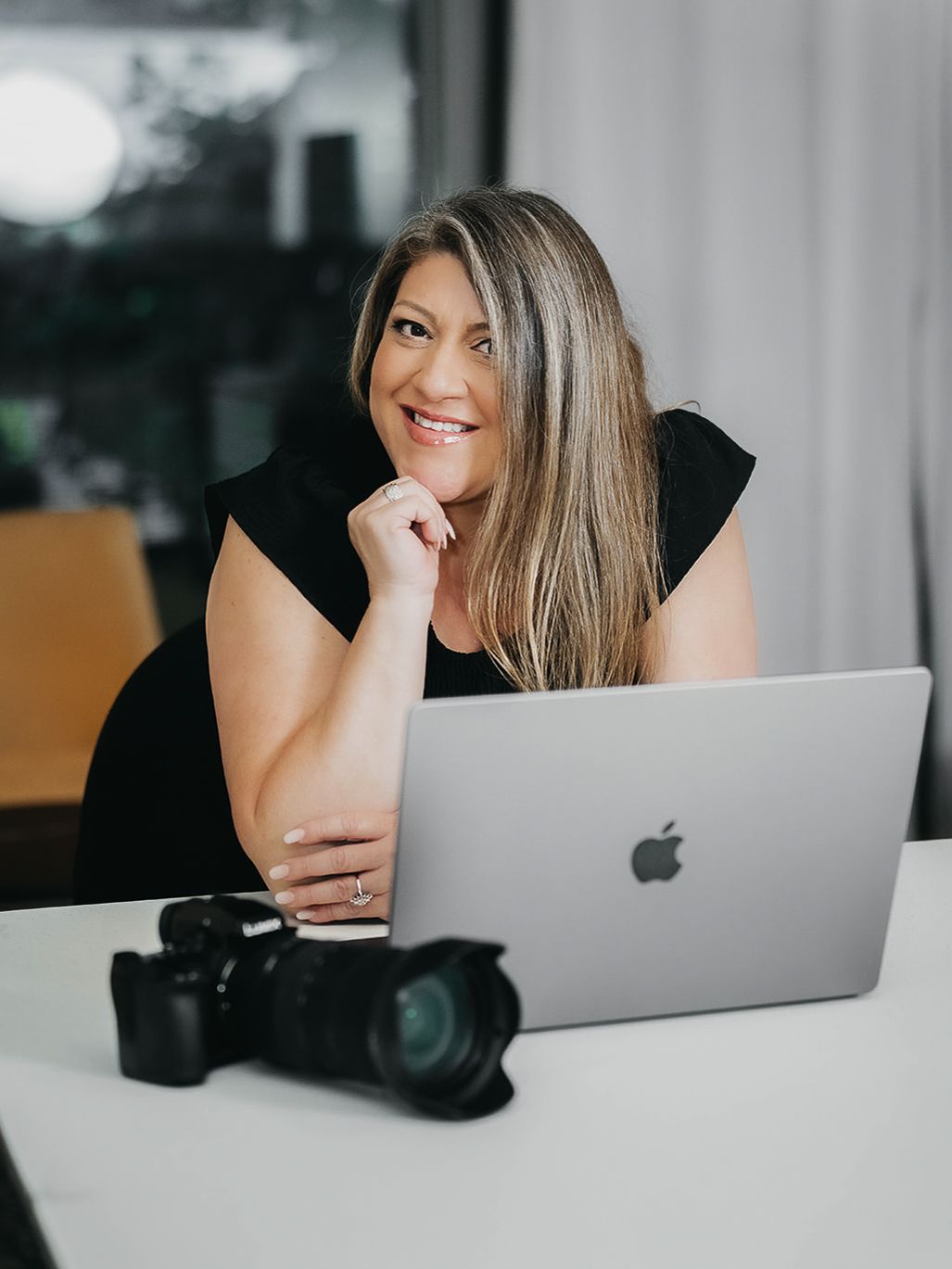 Creative professional working with laptop and camera equipment in bright office space.
