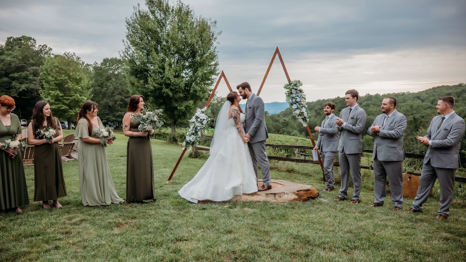 Panoramic view of a wedding celebration with guests gathered on a hillside.