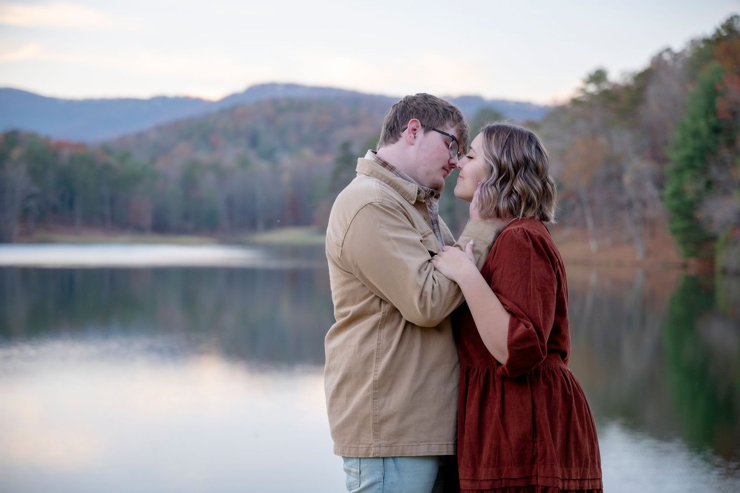 Lakeside engagement portrait with mountain landscape at sunset.