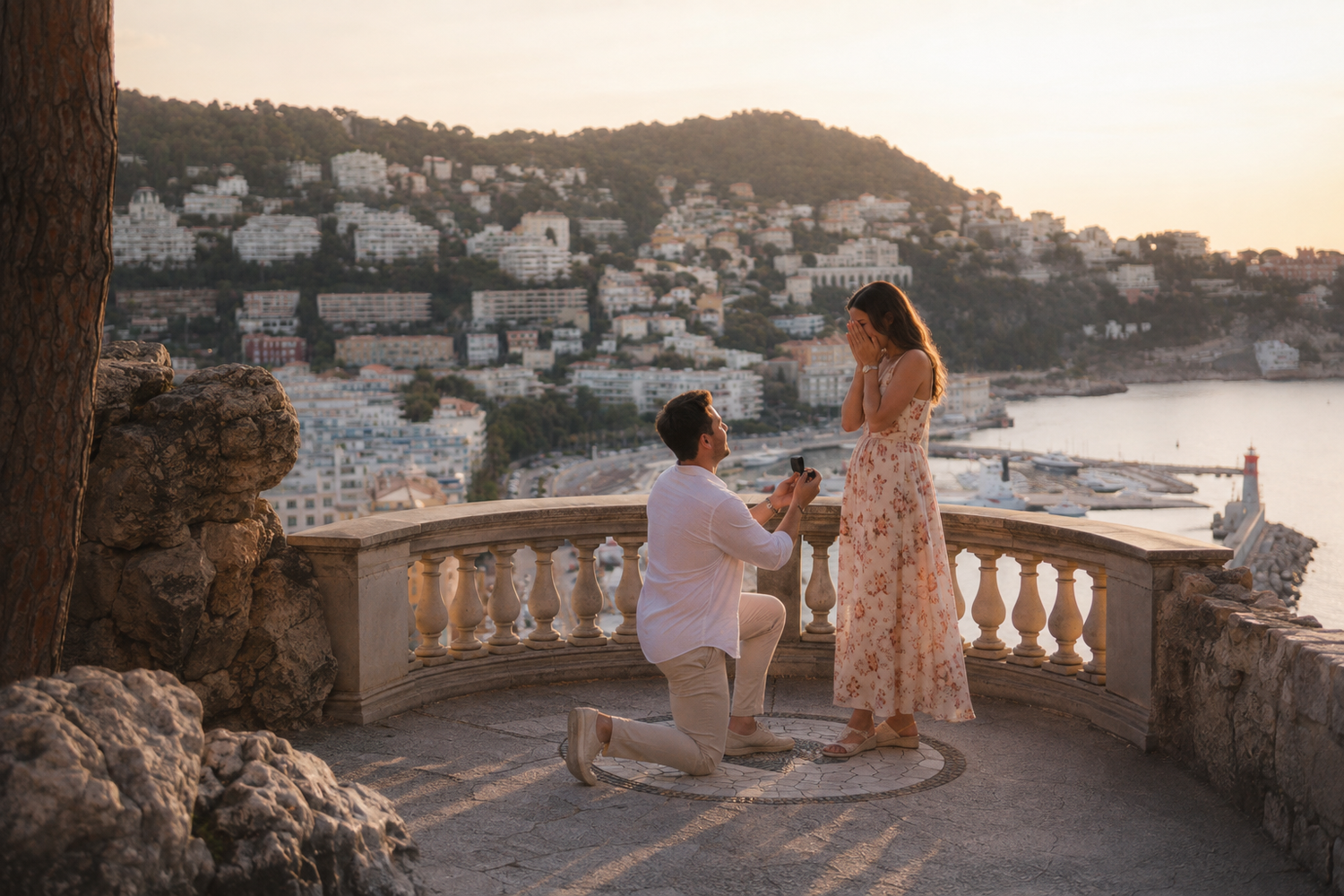 Man proposing to woman on scenic Mediterranean terrace at sunset with coastal town backdrop.